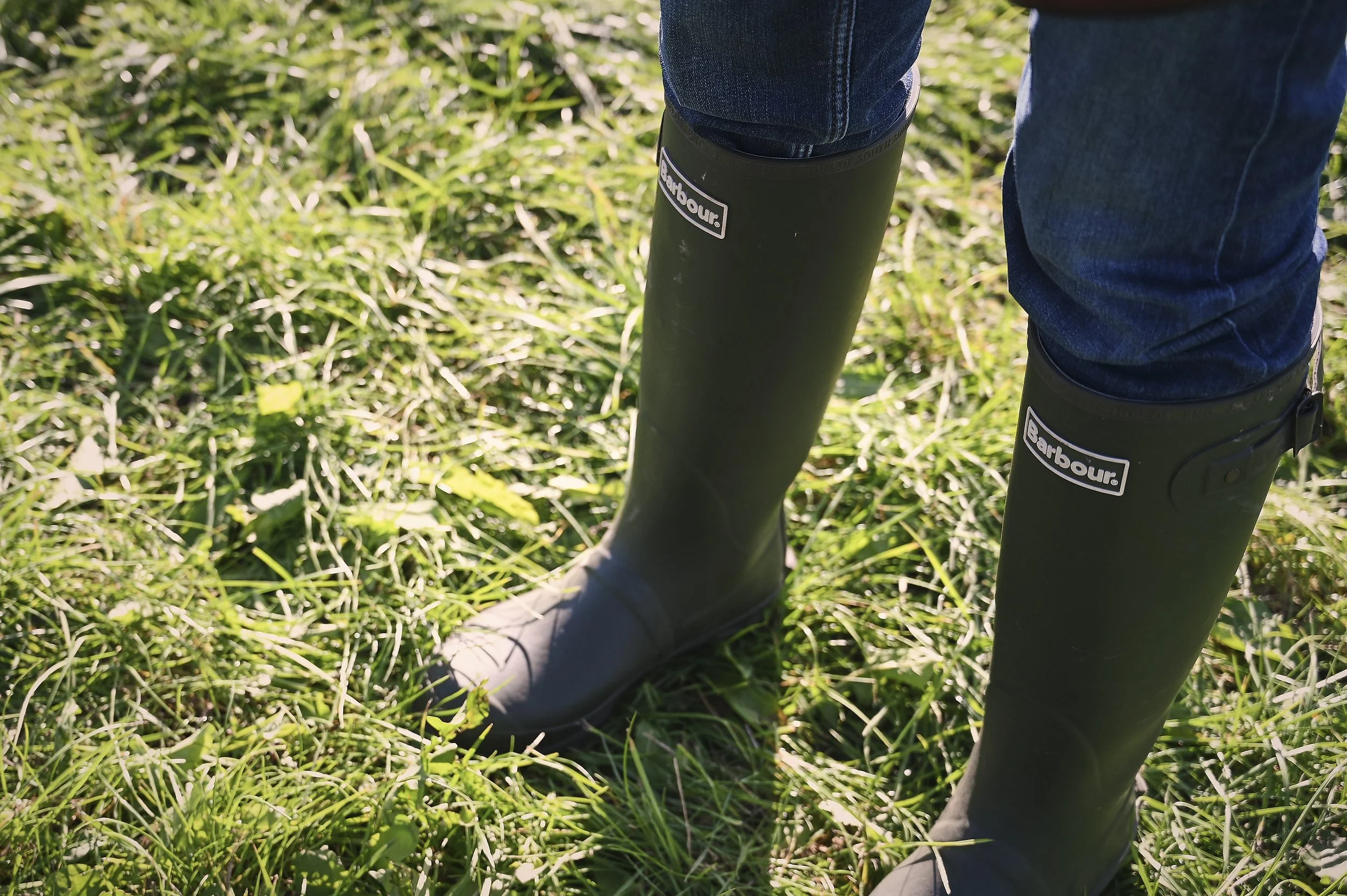 Person wearing black Barbour rain boots standing on green grass.