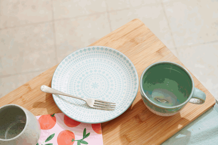 Empty patterned plate, fork, and mug on a wooden cutting board with a napkin featuring orange fruit illustrations.