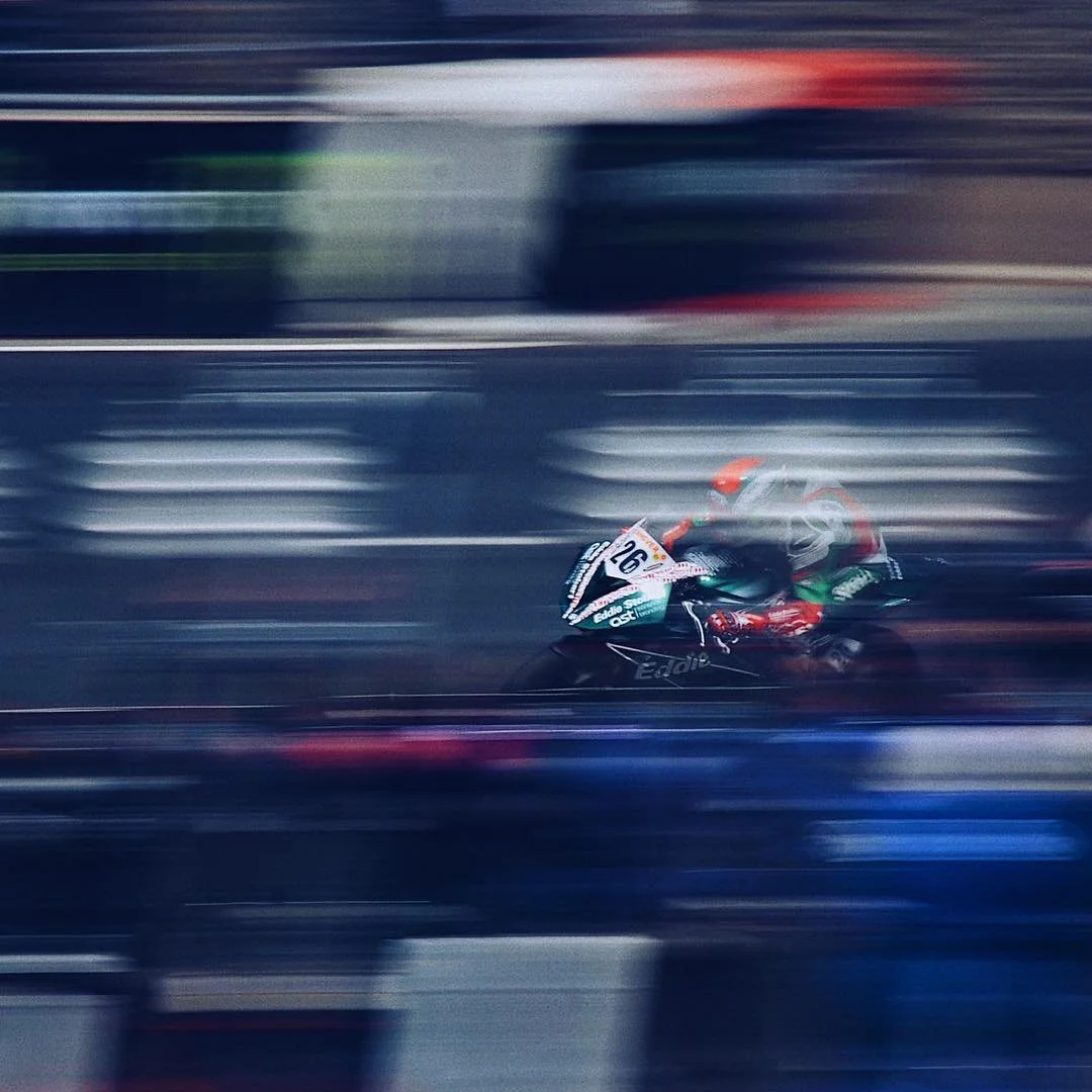A motorcycle racer in a racing suit and helmet speeding on a track, with motion blur in the background.