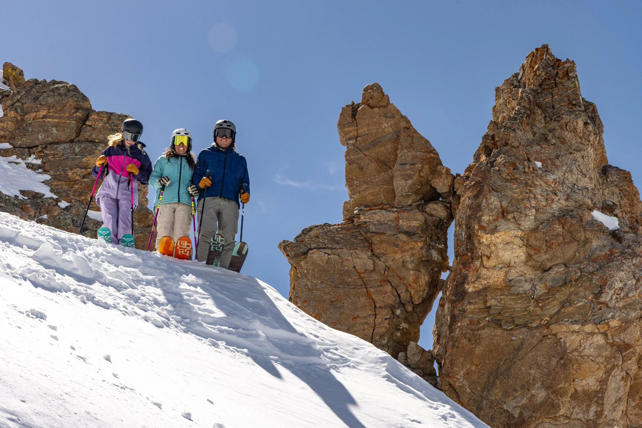 Three skier at the top of a slope, with rocks in the background