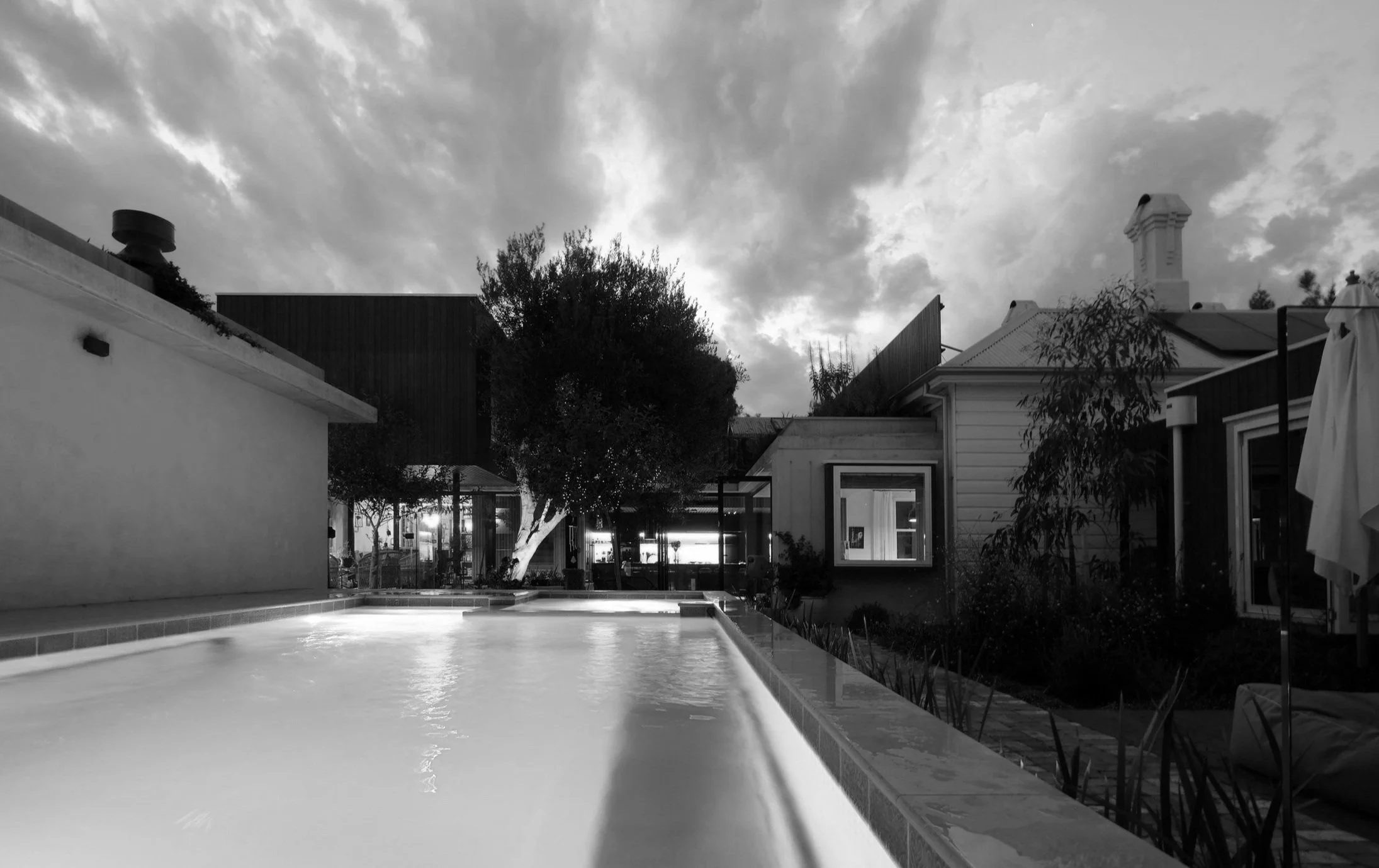 A backyard scene at dusk featuring a swimming pool, trees, and houses with clouds in the sky.