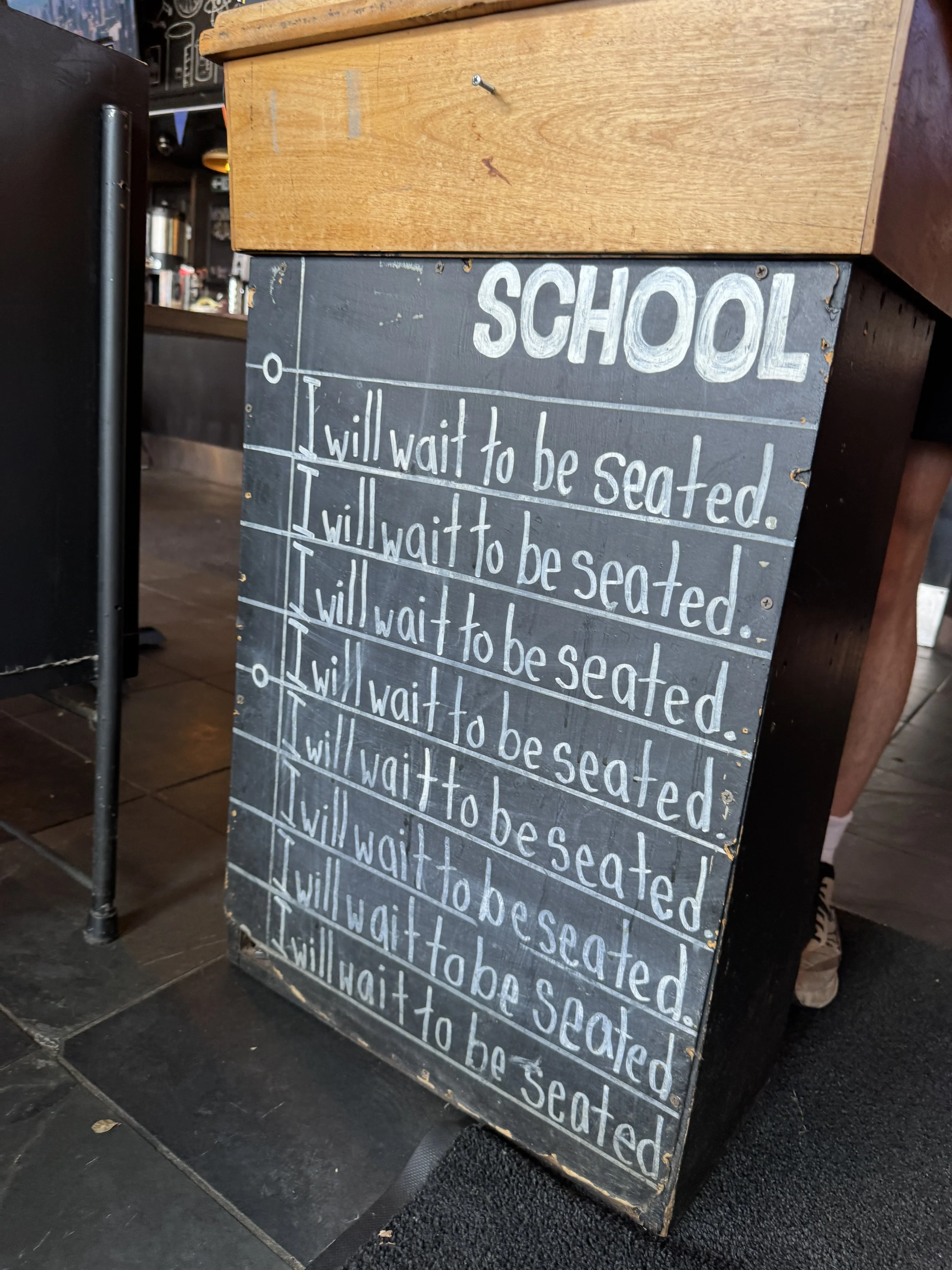 Chalkboard wait-to-be-seated sign at the entrance of SCHOOL Restaurant in Liberty Village, Toronto.
