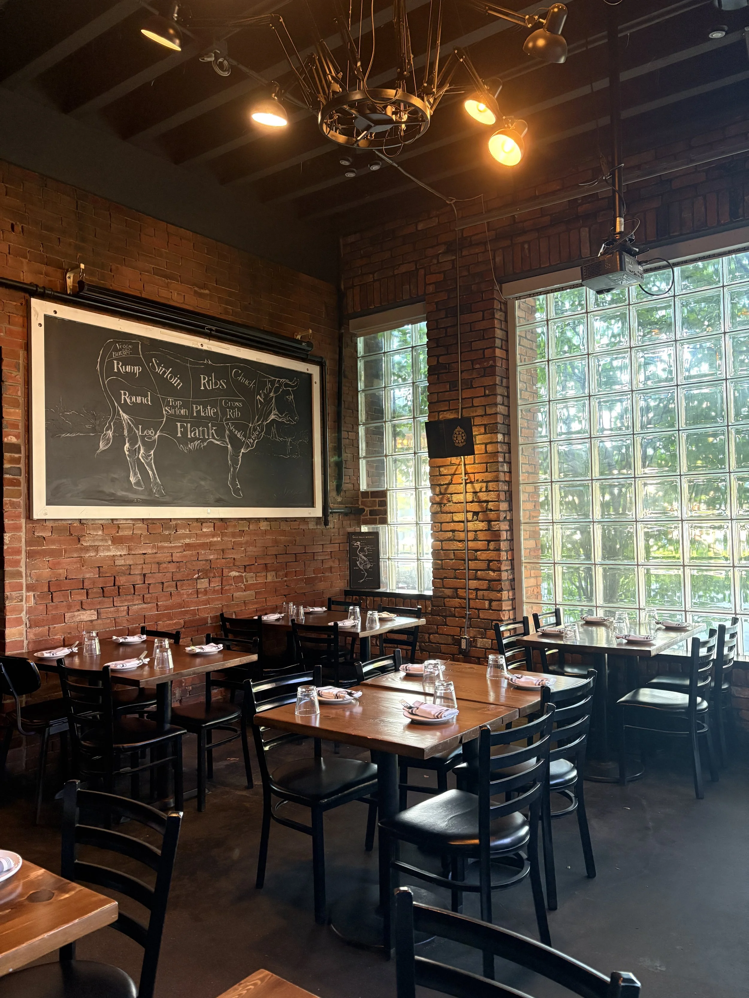 Interior dining room at SCHOOL Restaurant in Liberty Village, Toronto, with exposed brick walls, wooden tables and large windows.