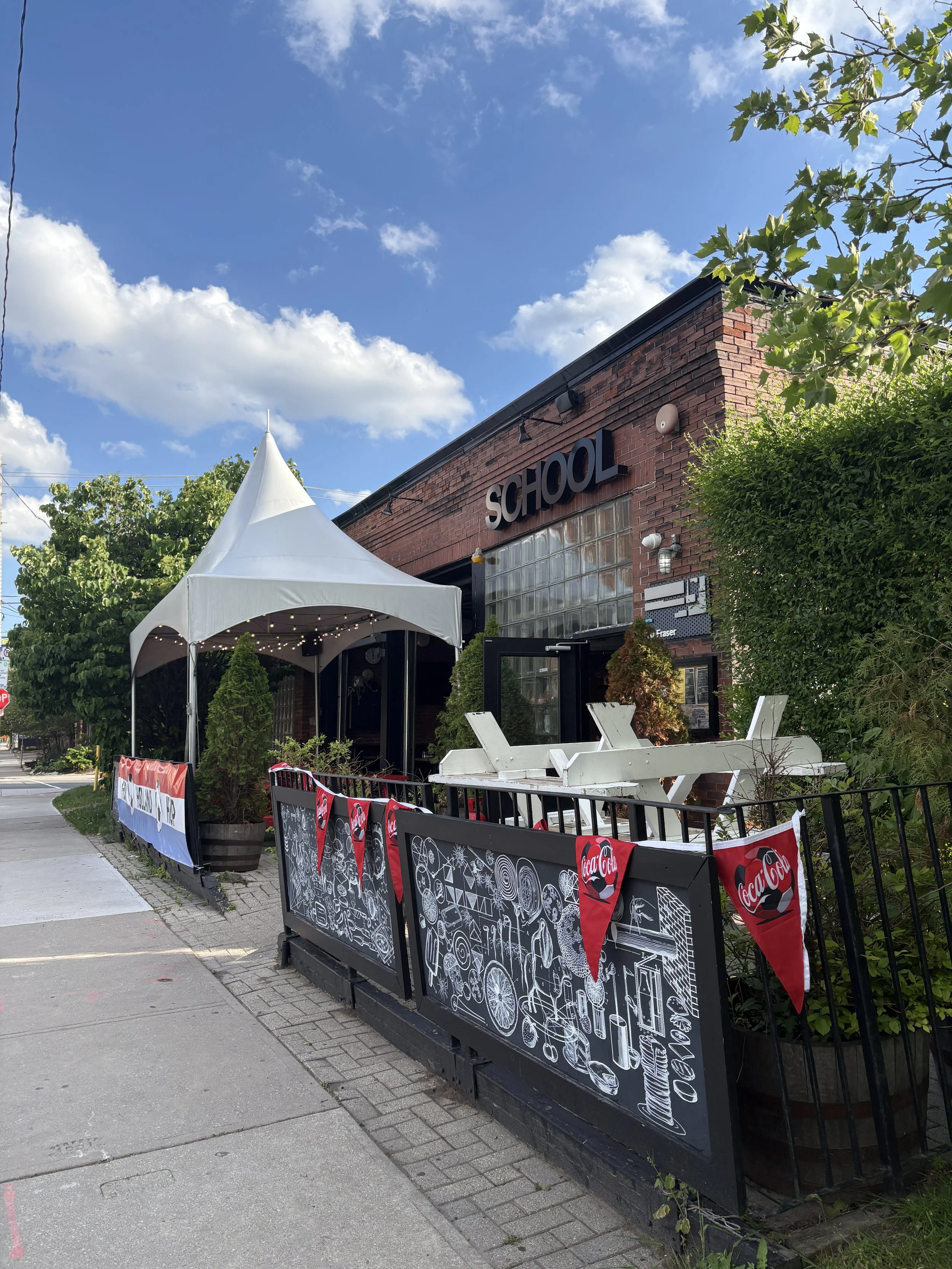 Exterior of SCHOOL Restaurant in Liberty Village, Toronto, showing the brick building and front patio along Fraser Avenue.