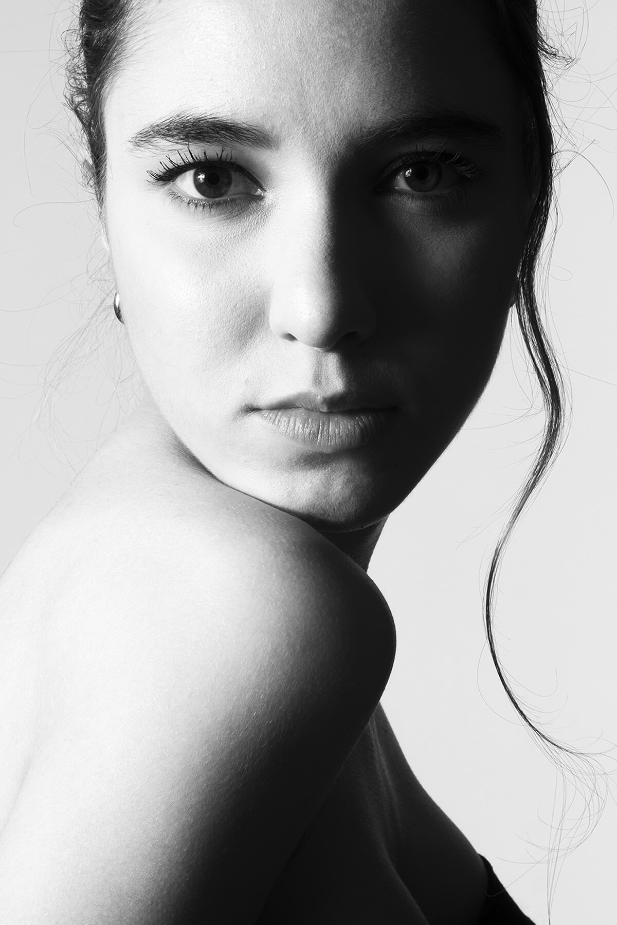 Retrato en blanco y negro de una mujer joven con expresión seria, con cabello recogido y un mechón suelto en un lado, mirando hacia la cámara.