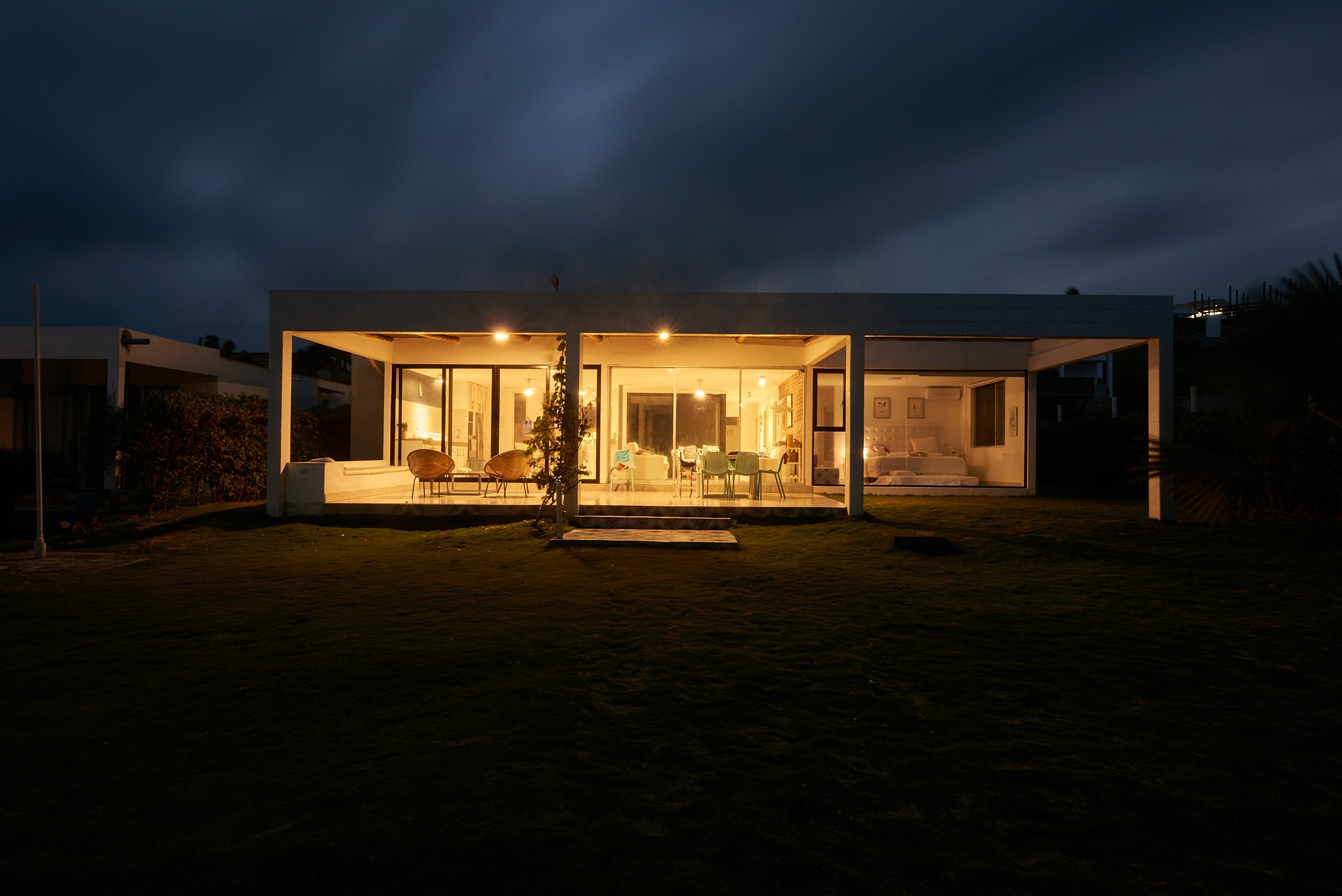 Casa moderna iluminada en la noche, con grandes ventanas y un patio de césped