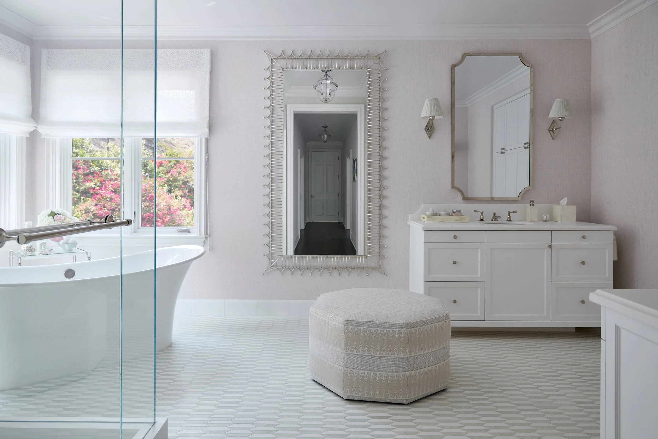 Ornate and elegant bathroom with large tub, glass shower, custom sink, and seating poof.