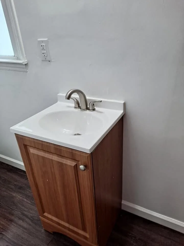 small room with a utility sink, wooden cabinet, white walls, and an electrical outlet