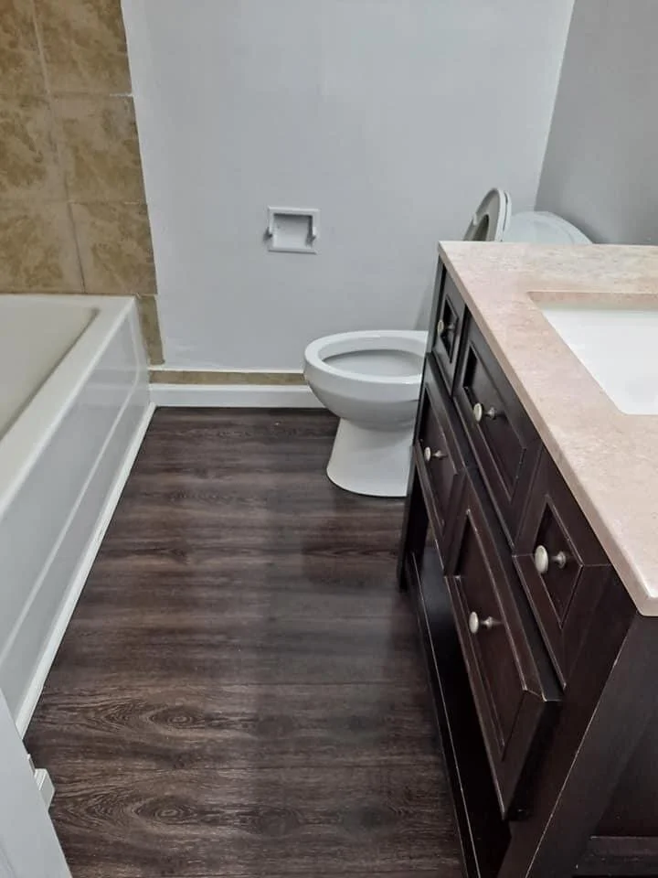Bathroom with a bathtub on the left, a toilet without a lid in the center, and a dark wood vanity with a beige countertop on the right.