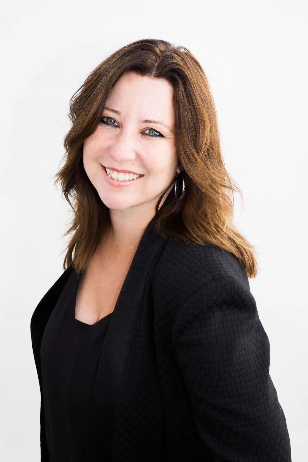 A woman with shoulder-length brown hair smiling, wearing a black top and blazer, against a white background.