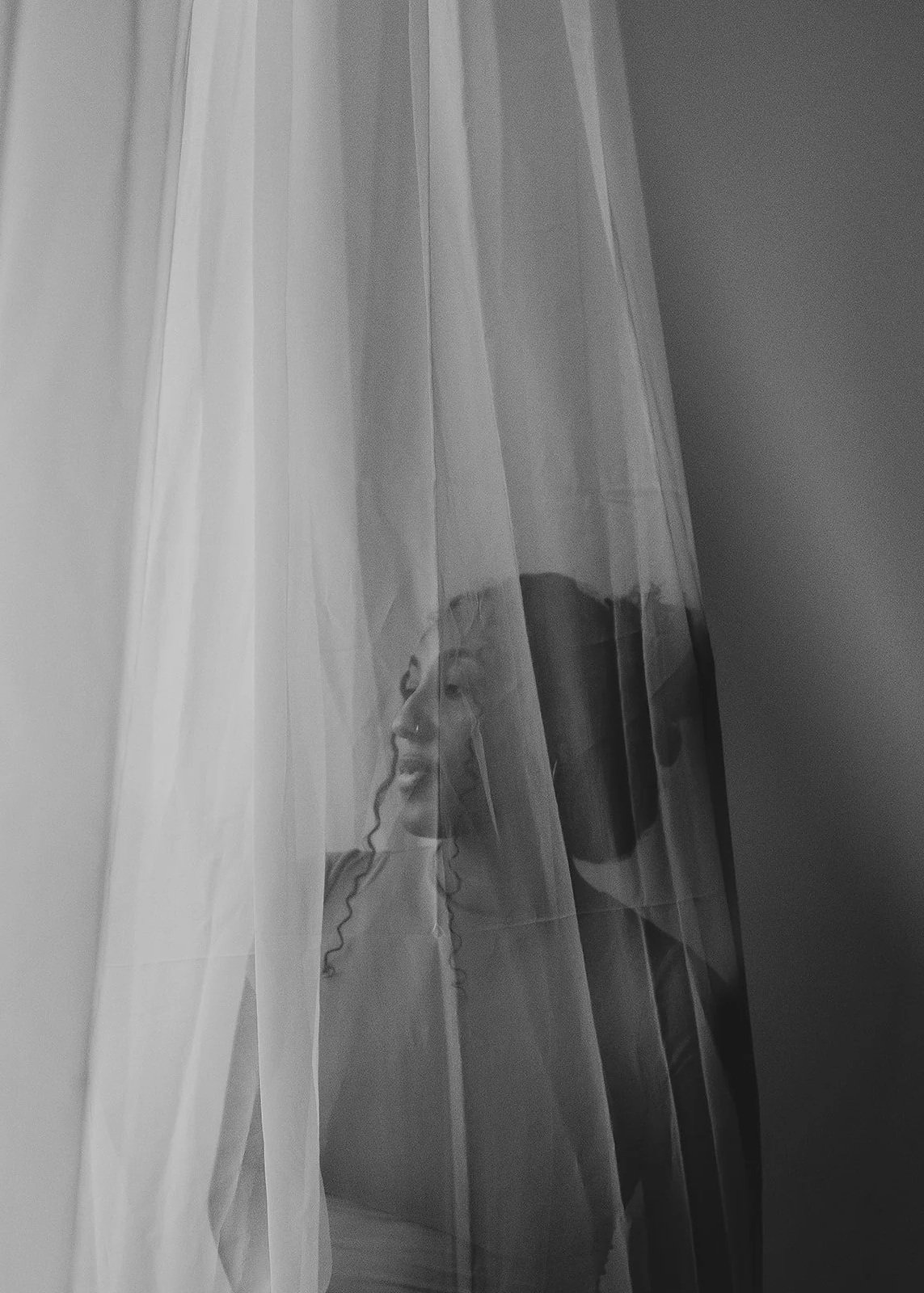 A woman with curly hair peering through a sheer curtain. House of Nicoline - HON - intuitive guidance, astrocartography, viberise - Jetta Nicoline Harrison