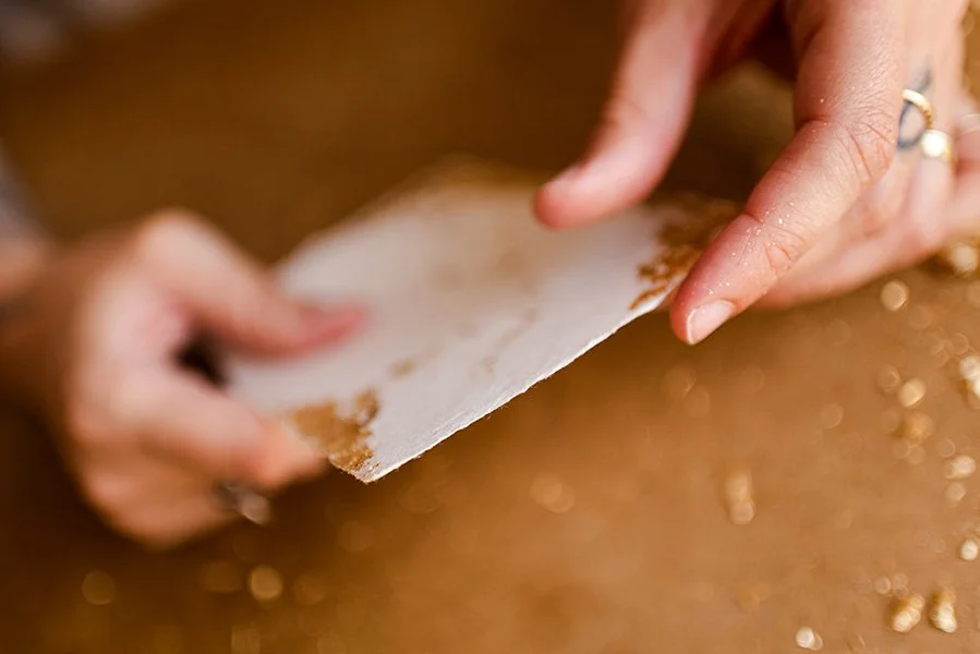 Mains appliquant des feuilles d'or sur une carte en papier fait-main — atelier Allons-y Alonso EmmanuelleBraun.jpg