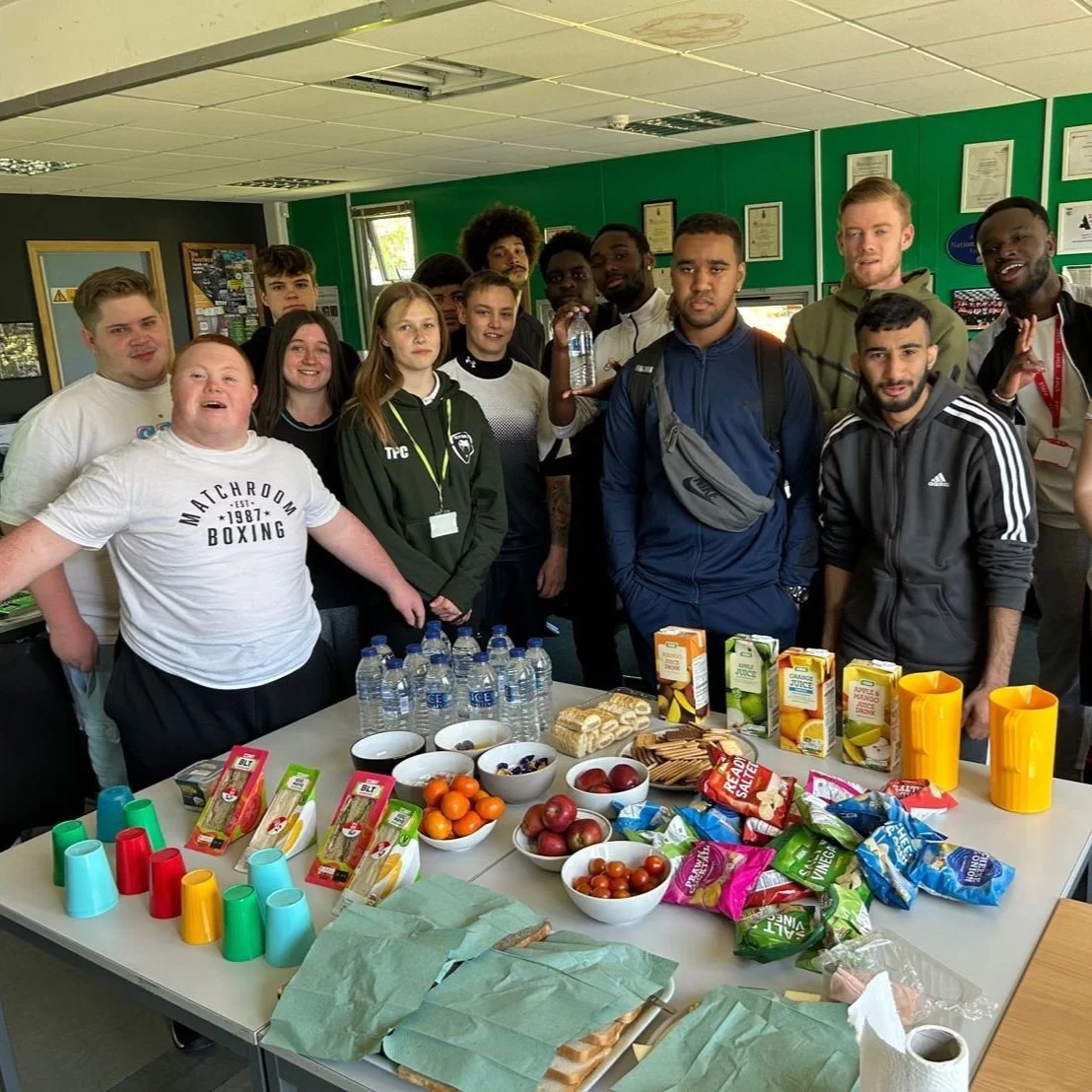 Group of young people gathered in a room with snacks and beverages on a table, smiling at the camera.