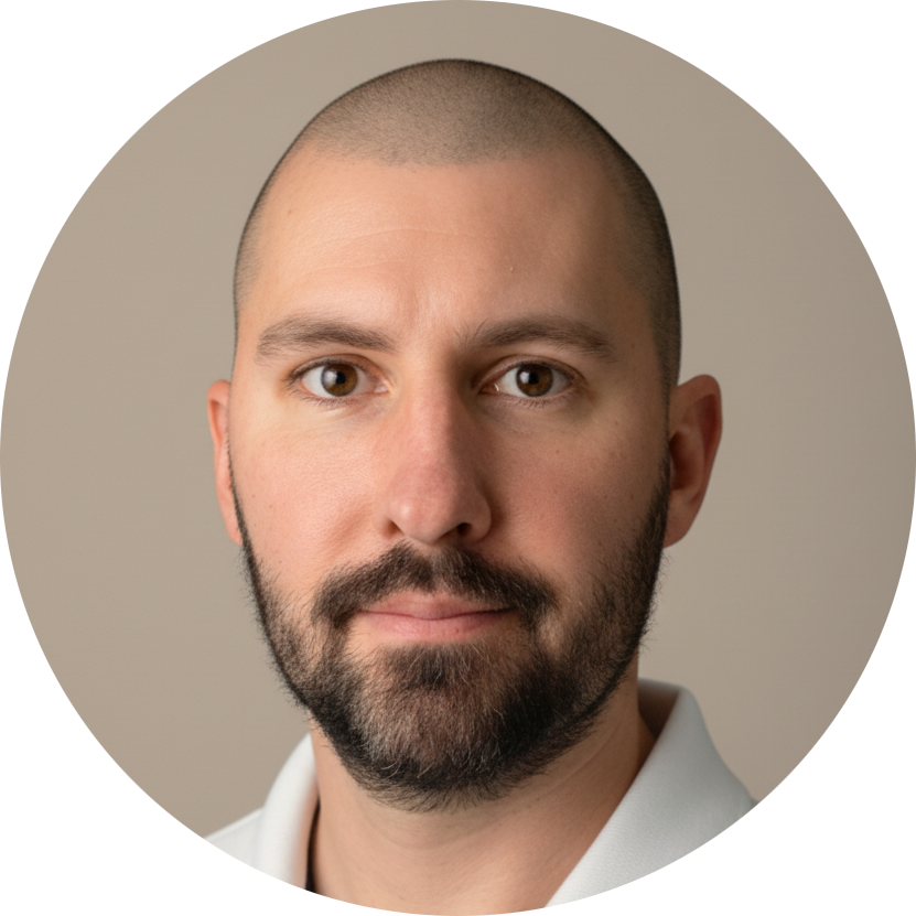 Porträtt av en man med skägg och ett nära leende, vit skjorta, bild mot en neutral bakgrund.