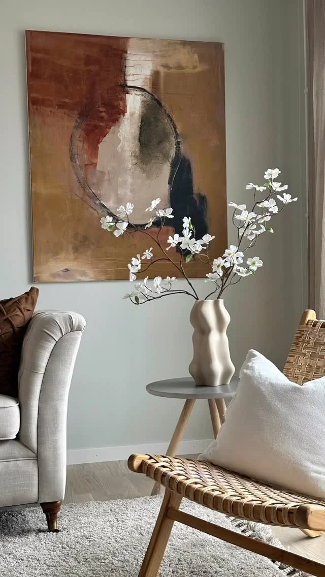 Växt med vita blommor i ett beige vaser på ett runt bord i ett vardagsrum.