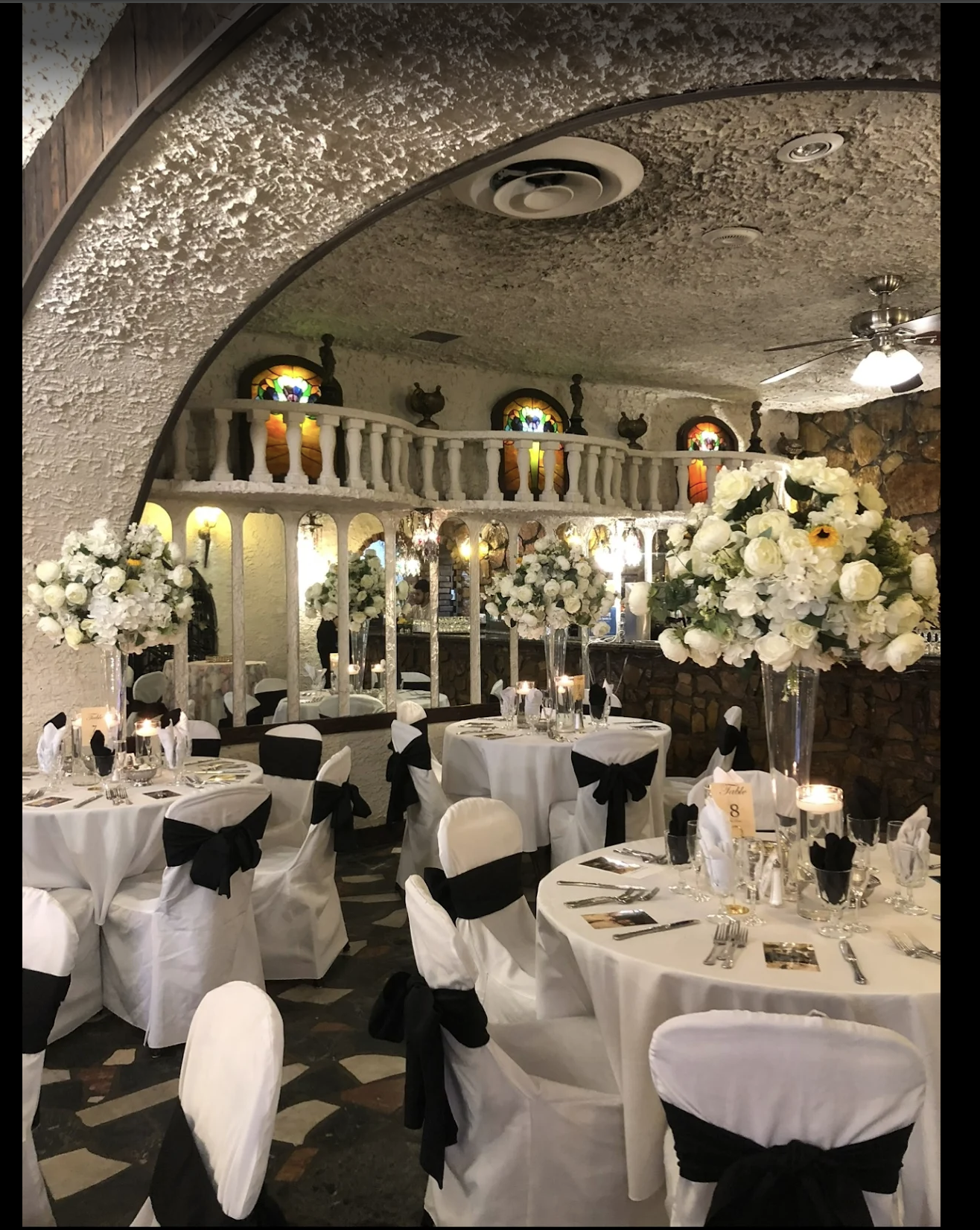 Small wedding reception room with round tables, white floral centerpieces, candles, and black-and-white décor.
