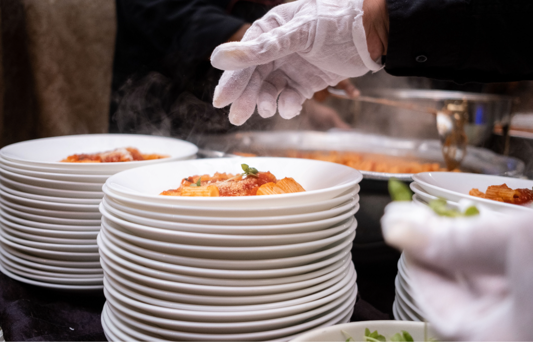 Banquet staff serving pasta into individual plates during event meal service.