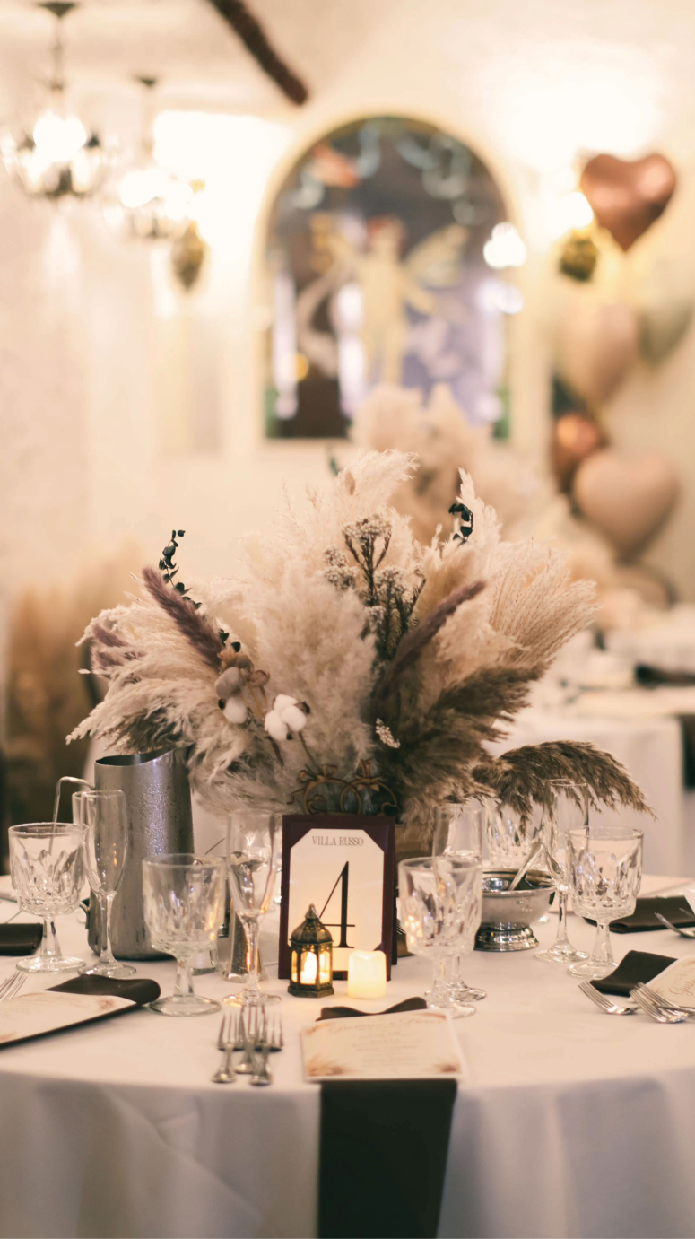 Wedding reception table with pampas grass centerpiece, candles, glassware, and place settings.
