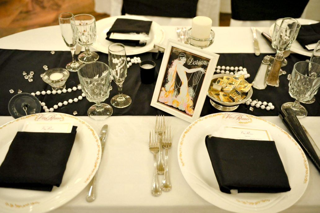1920s-themed banquet table set with black linens, pearl accents, glassware, and vintage décor.