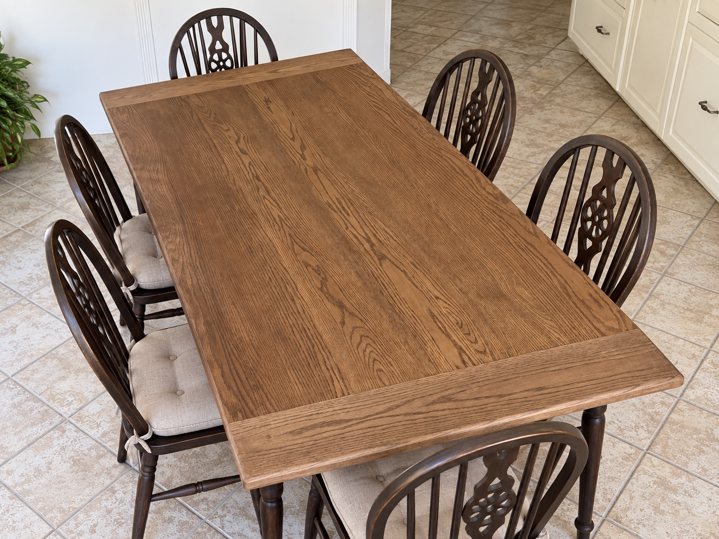 Wood dining table with six chairs, beige cushioned seats, in a tiled kitchen floor.