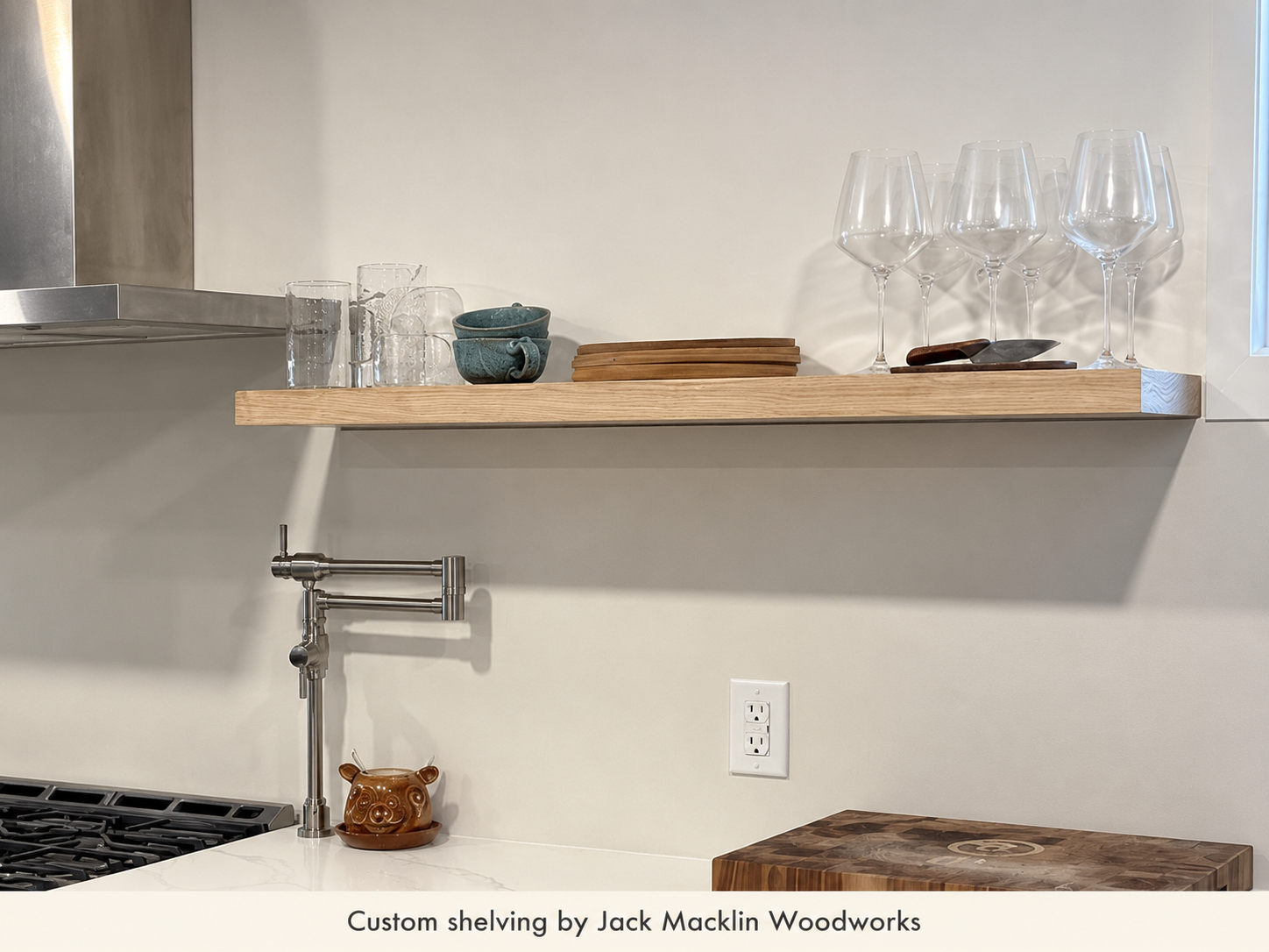A kitchen shelf with drinking glasses, bowls, cutting boards, and wine glasses. A pipe is visible below the shelf.