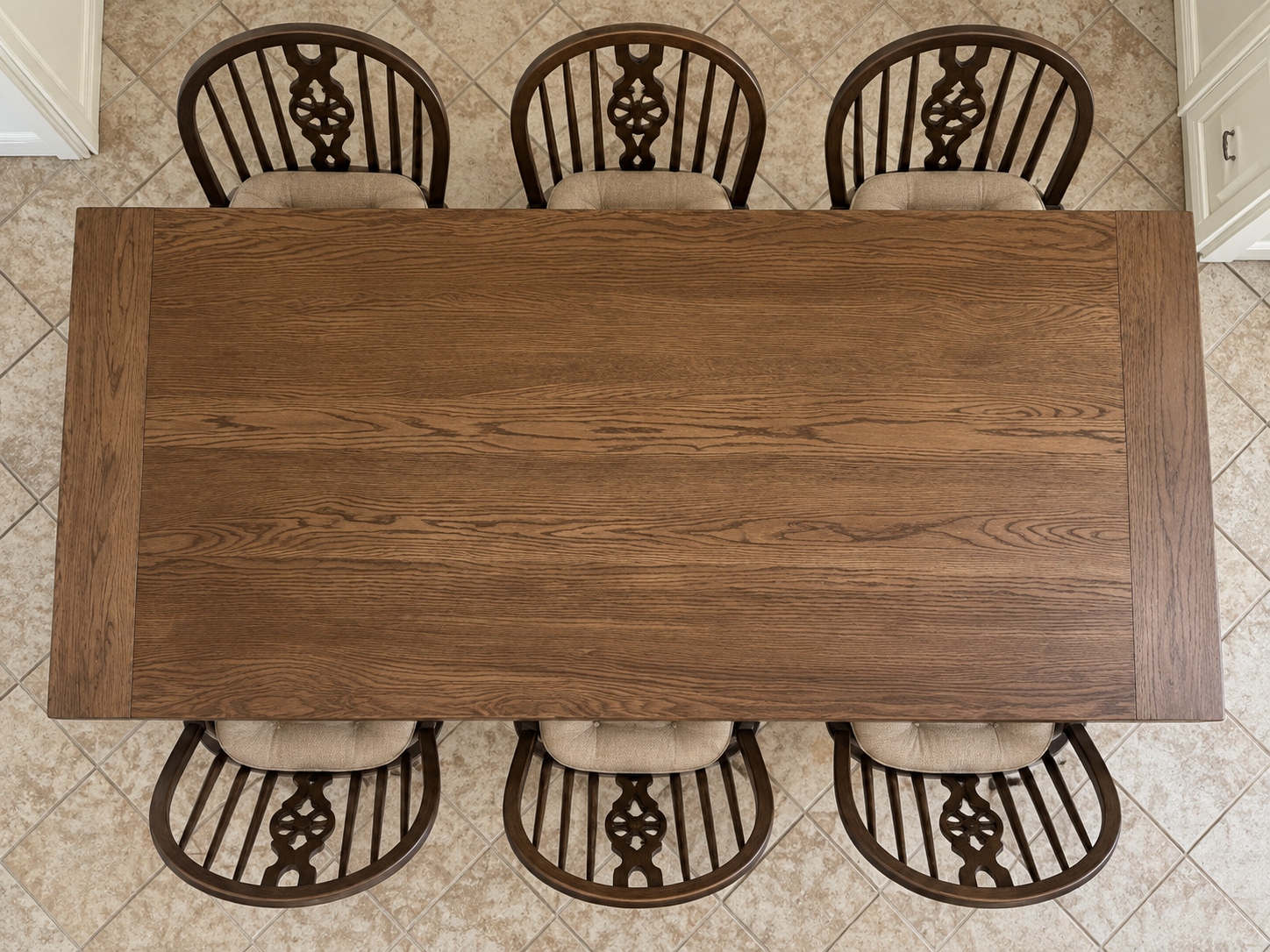 Overhead view of a wooden dining table with a rectangular top and six matching chairs with cushioned seats, set on a tiled floor.