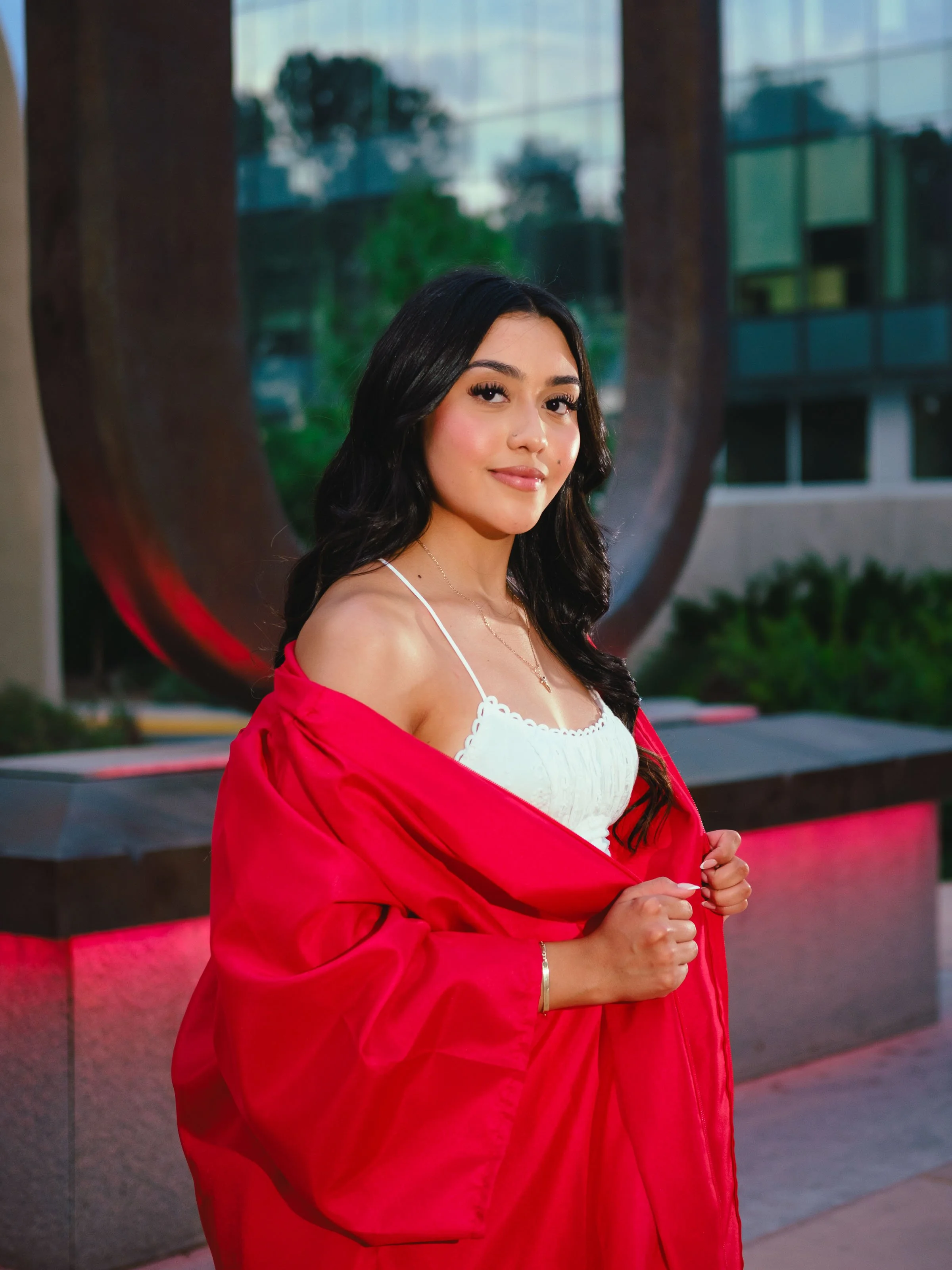 University of New Mexico graduate wearing a red graduation gown over a white dress posing near the Big U during a UNM graduation photography session in Albuquerque.