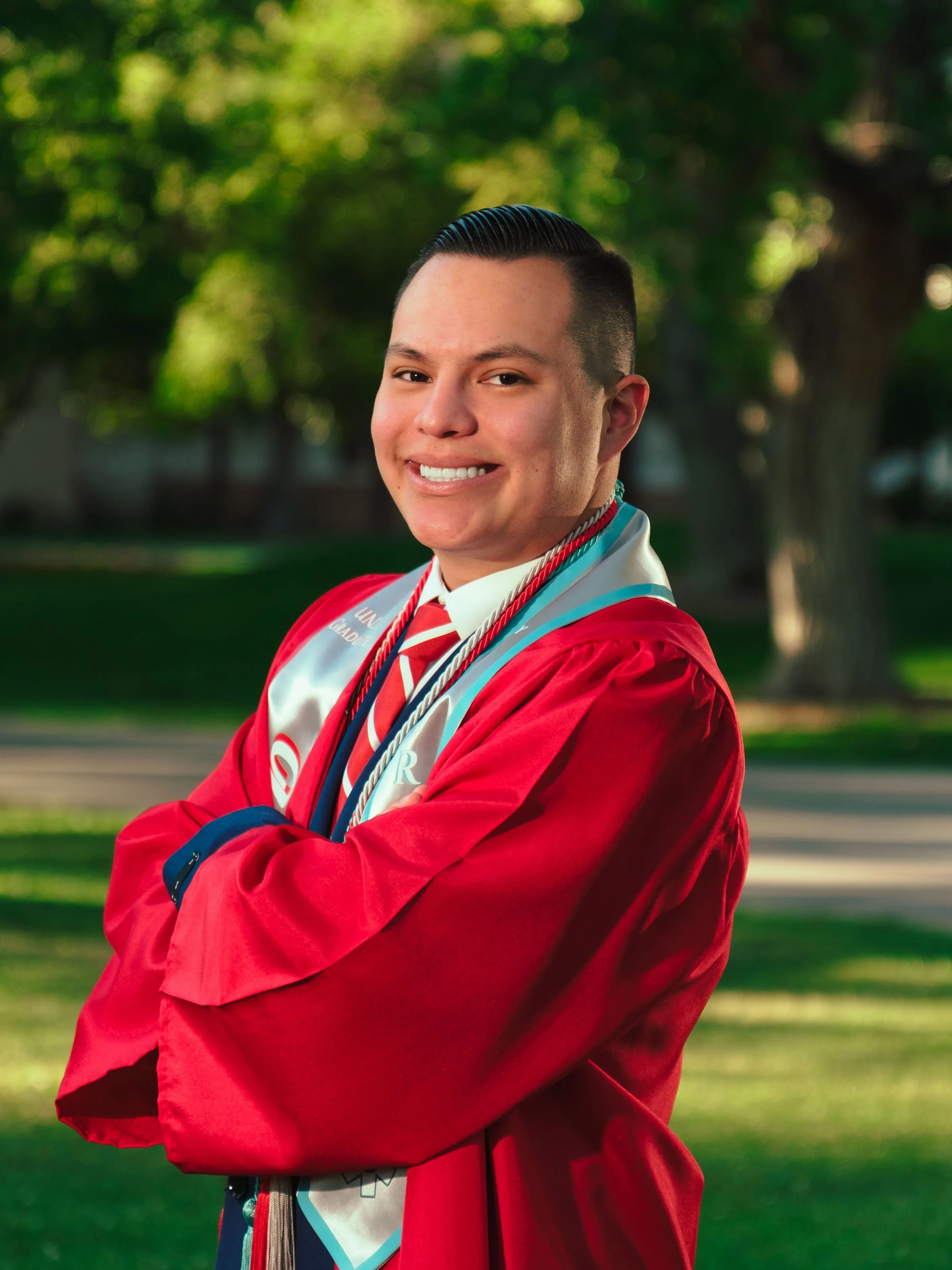 UNM graduate wearing a red cap and gown with graduation cords and stole during a University of New Mexico graduation portrait session in Albuquerque.