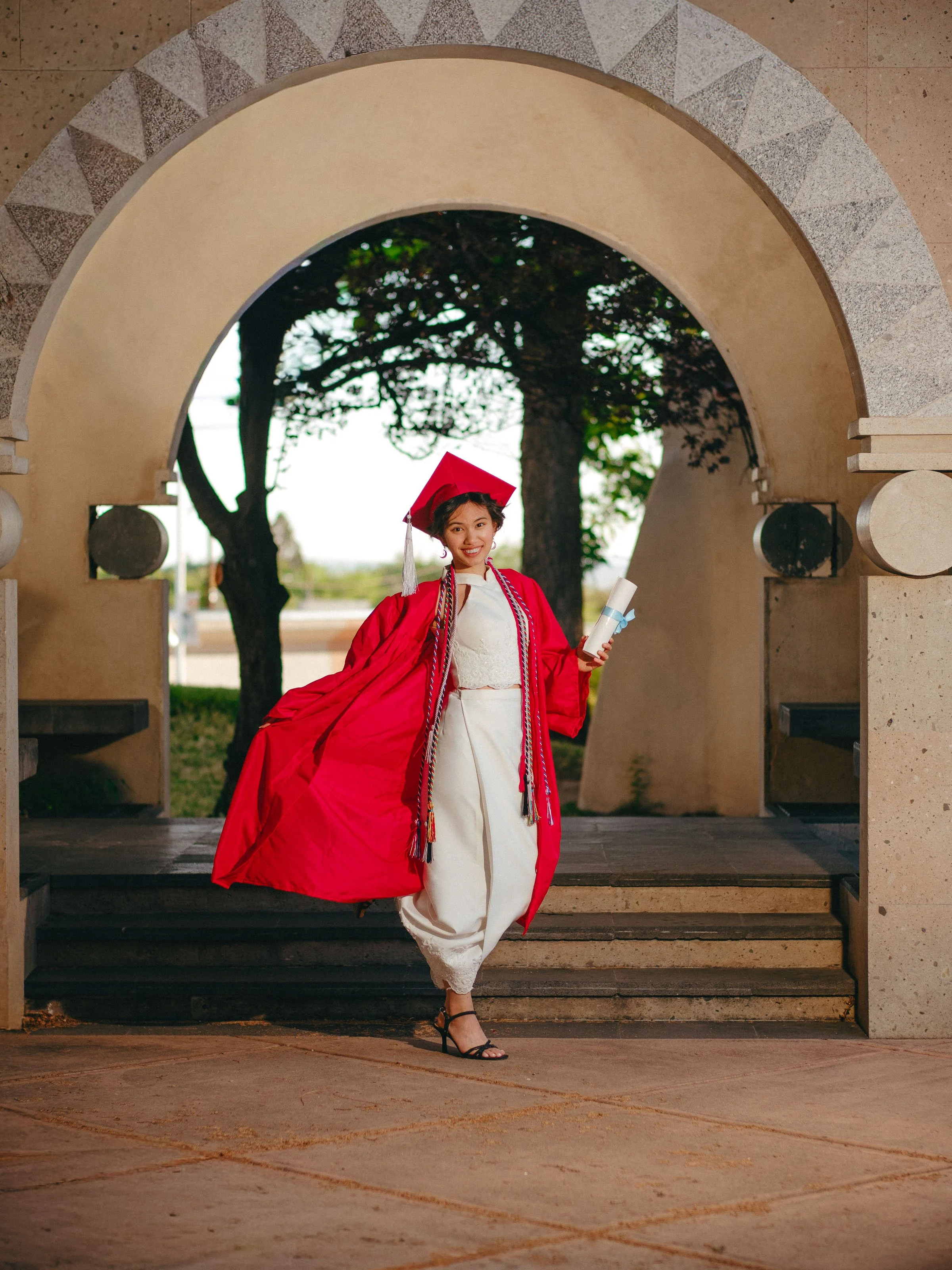 University of New Mexico graduate walking beneath a campus arch in red cap and gown during a UNM graduation photoshoot in Albuquerque, New Mexico.