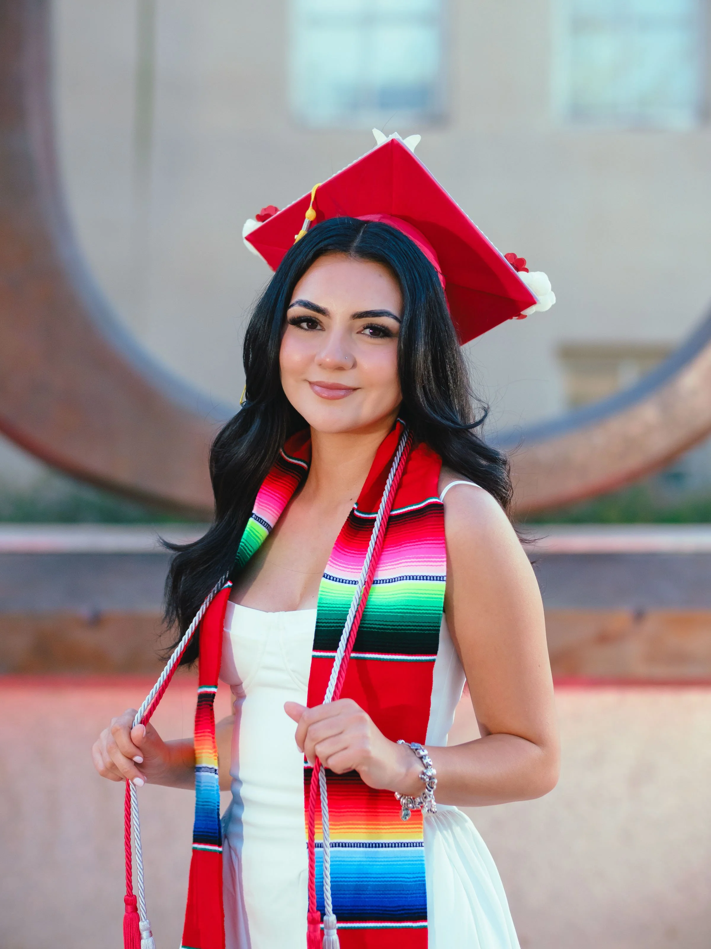 University of New Mexico graduate wearing a Centro de la Raza stole and red graduation cap during a UNM graduation portrait session in Albuquerque, celebrating her Raza Stoling Ceremony.