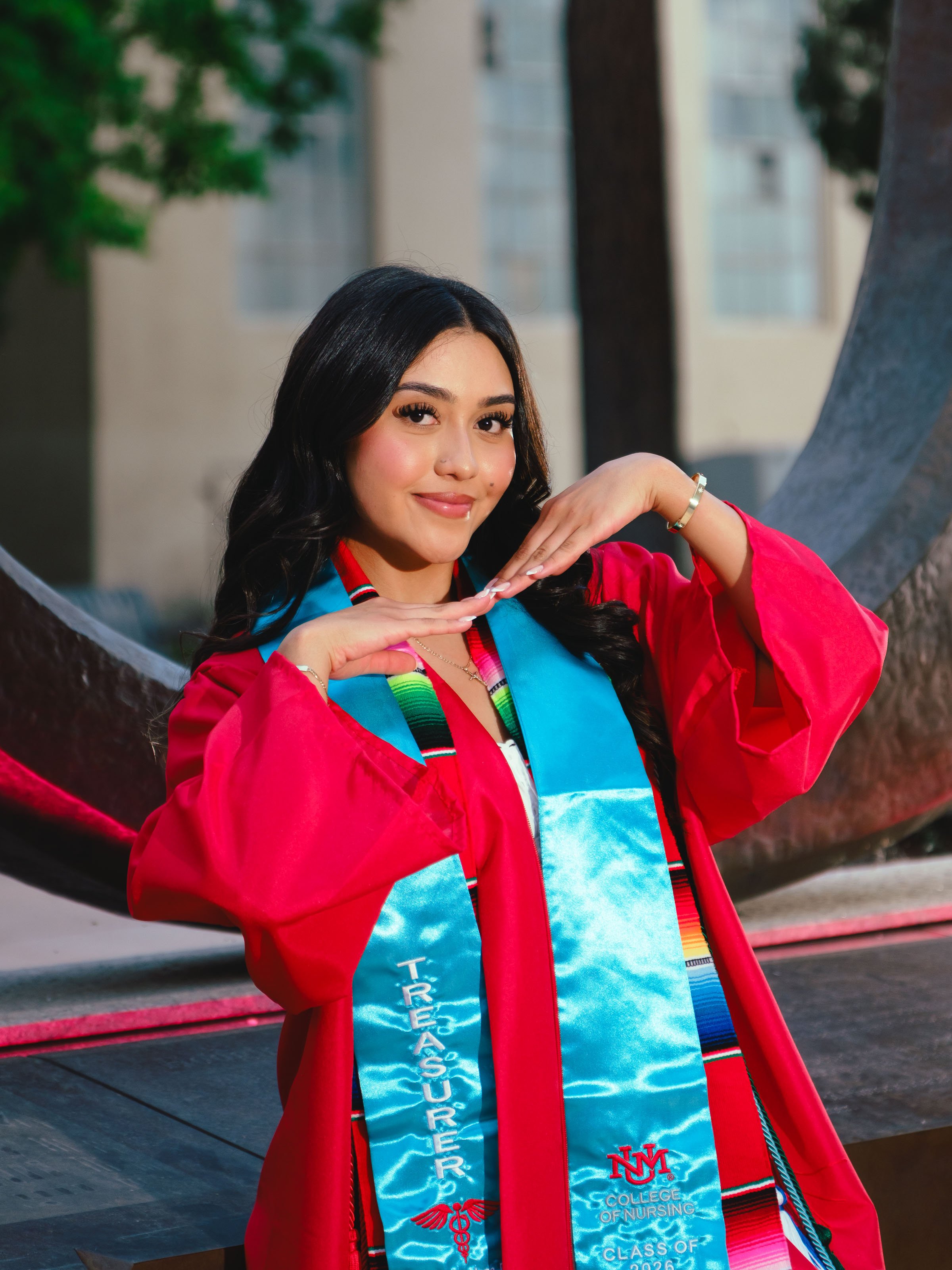 UNM graduate wearing a Centro de la Raza stole and red cap and gown during a University of New Mexico Raza Stoling Ceremony graduation portrait session in Albuquerque.