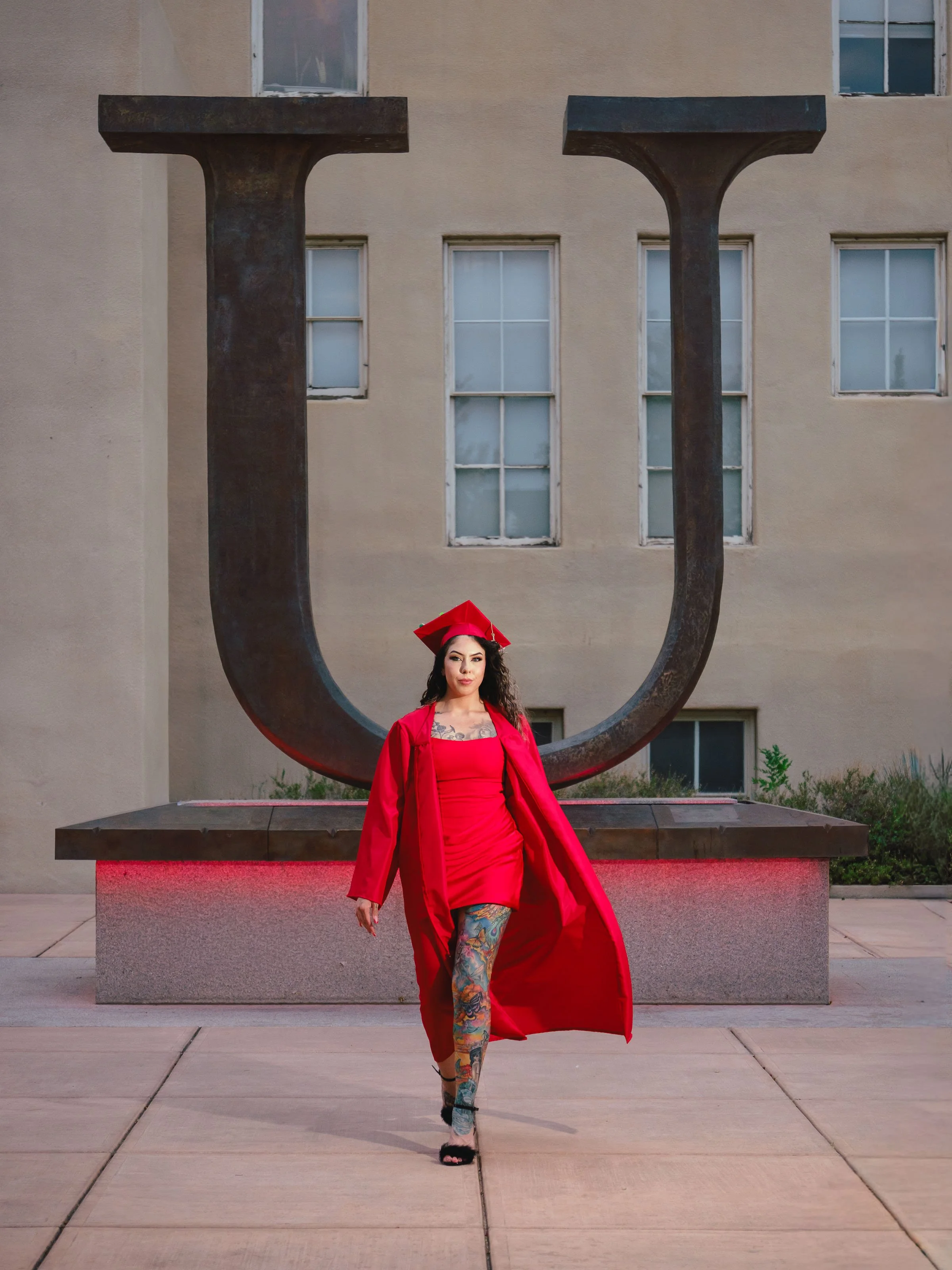 University of New Mexico graduate in a red cap and gown walking in front of the iconic Big U during a UNM graduation photo session in Albuquerque.