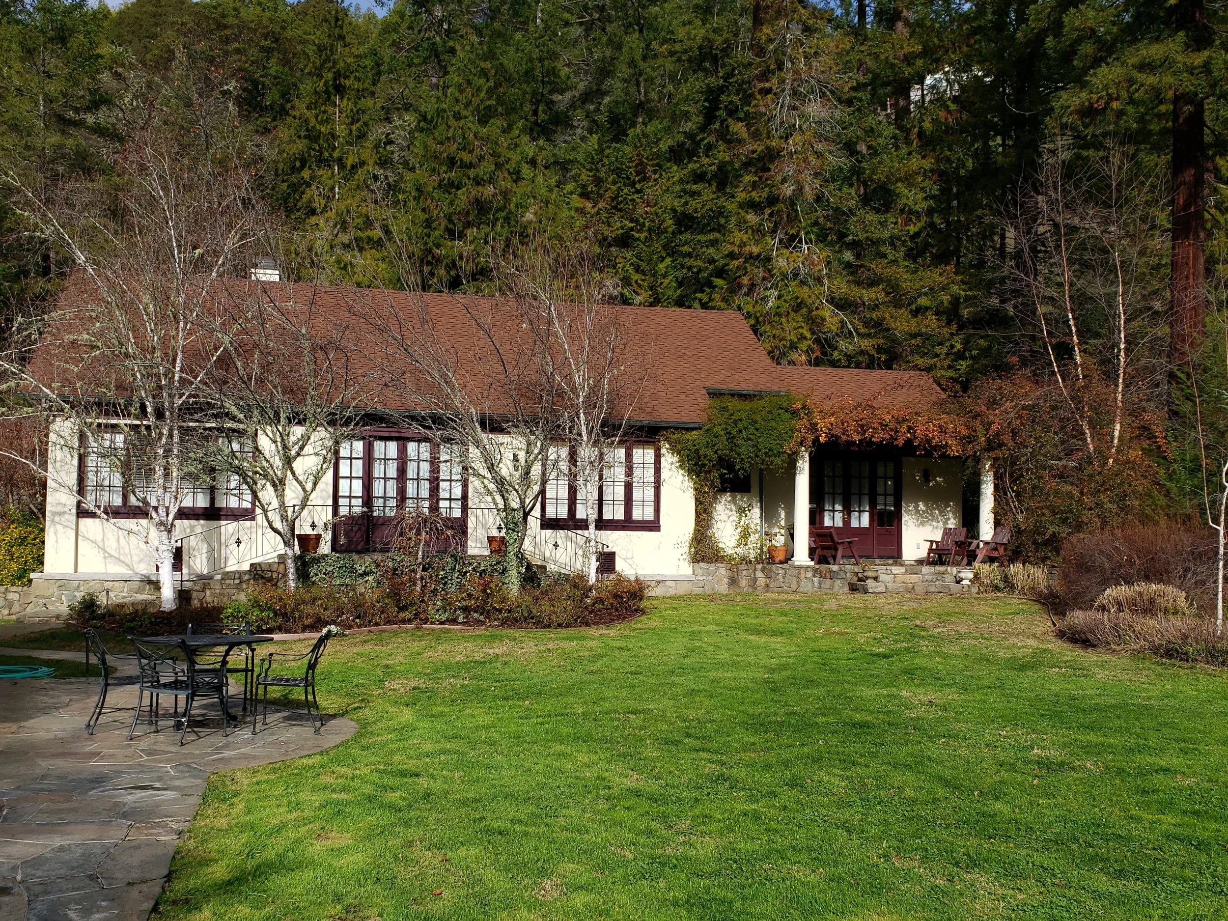 The cottage house with a red-tiled roof and white walls, surrounded by trees.