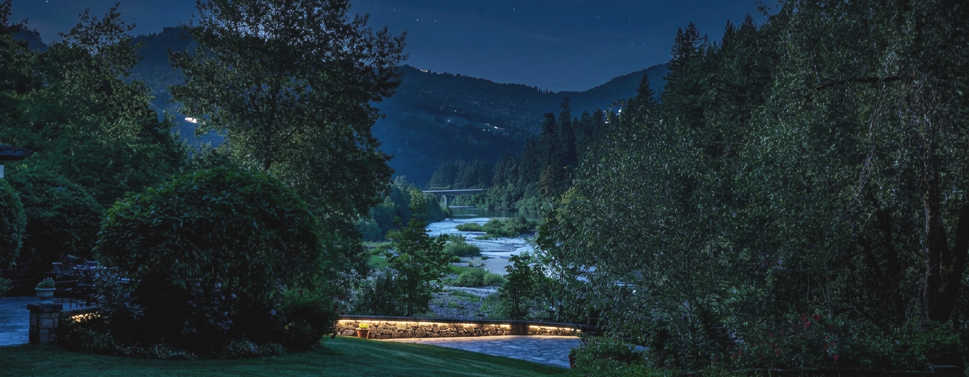 Nighttime view of a lush green landscape with trees, the Eel river, and mountains in the background, illuminated by moonlight.