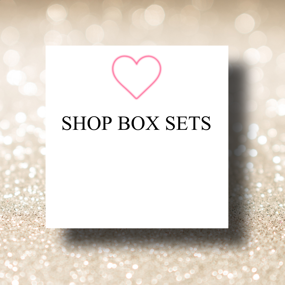 White square with black text 'Shop Box Sets' and a pink heart outline above, on a glittery beige background.
