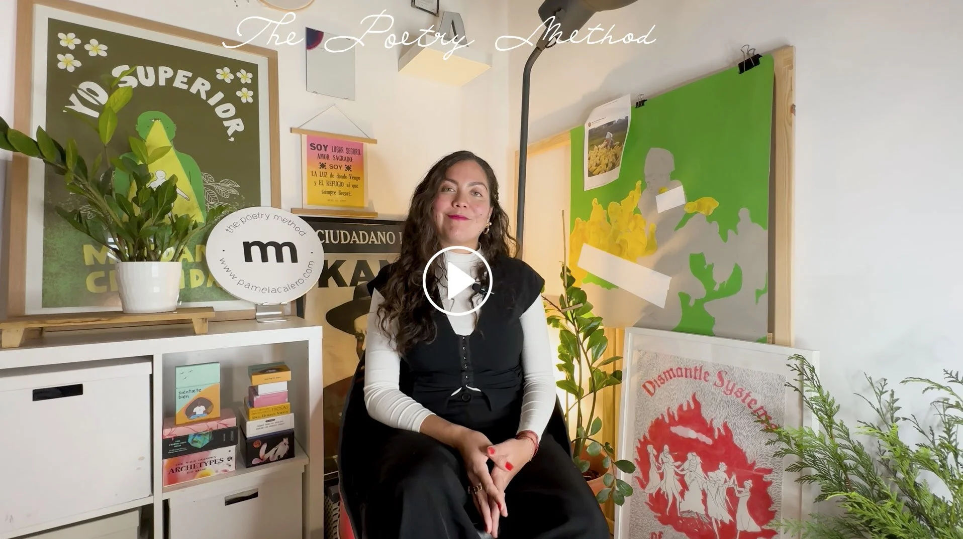 Pamela Calero sitting on a chair in a room decorated with posters and plants, smiling at the camera.