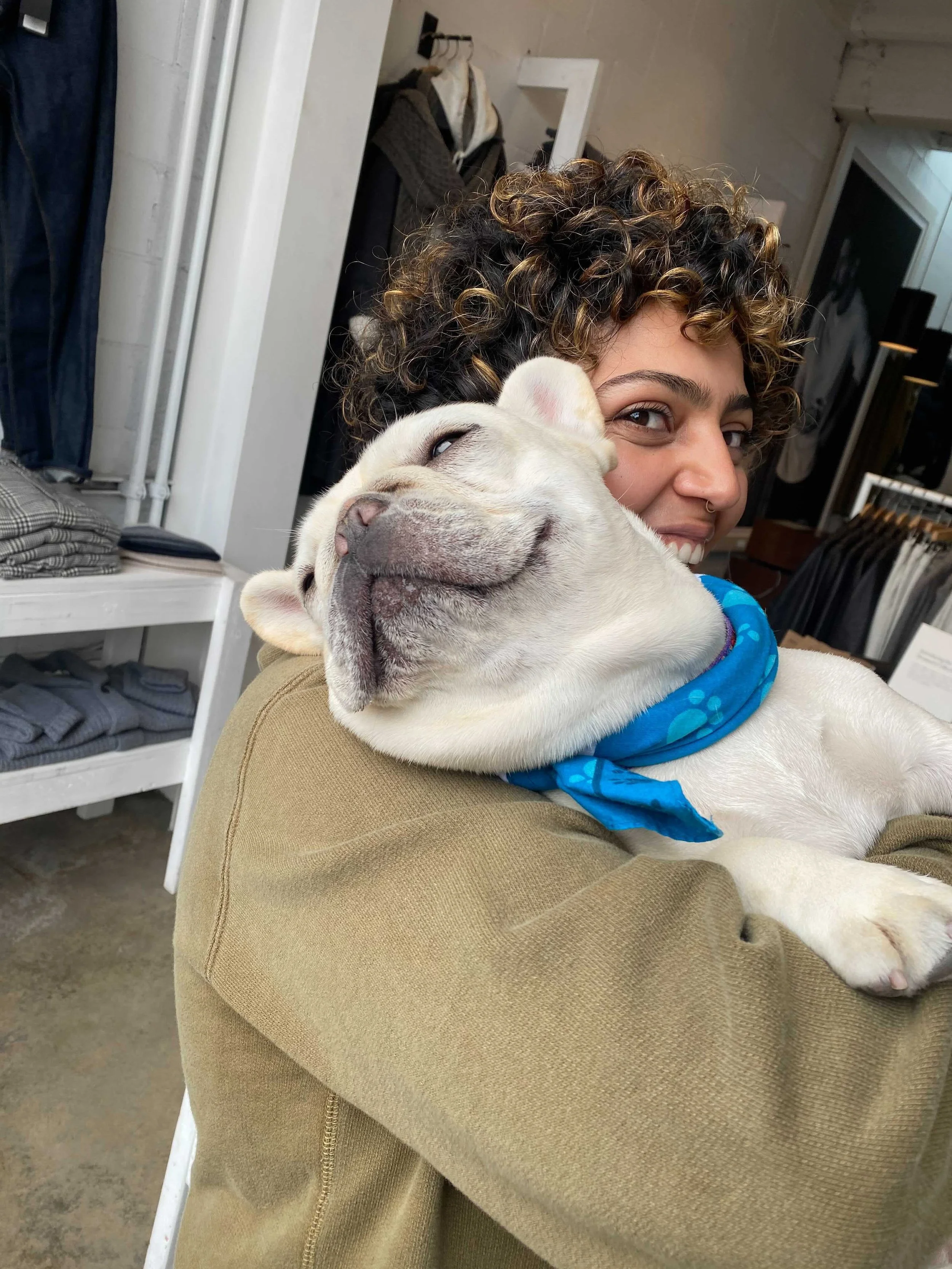 A person with curly brown hair hugs a small white dog to their chest