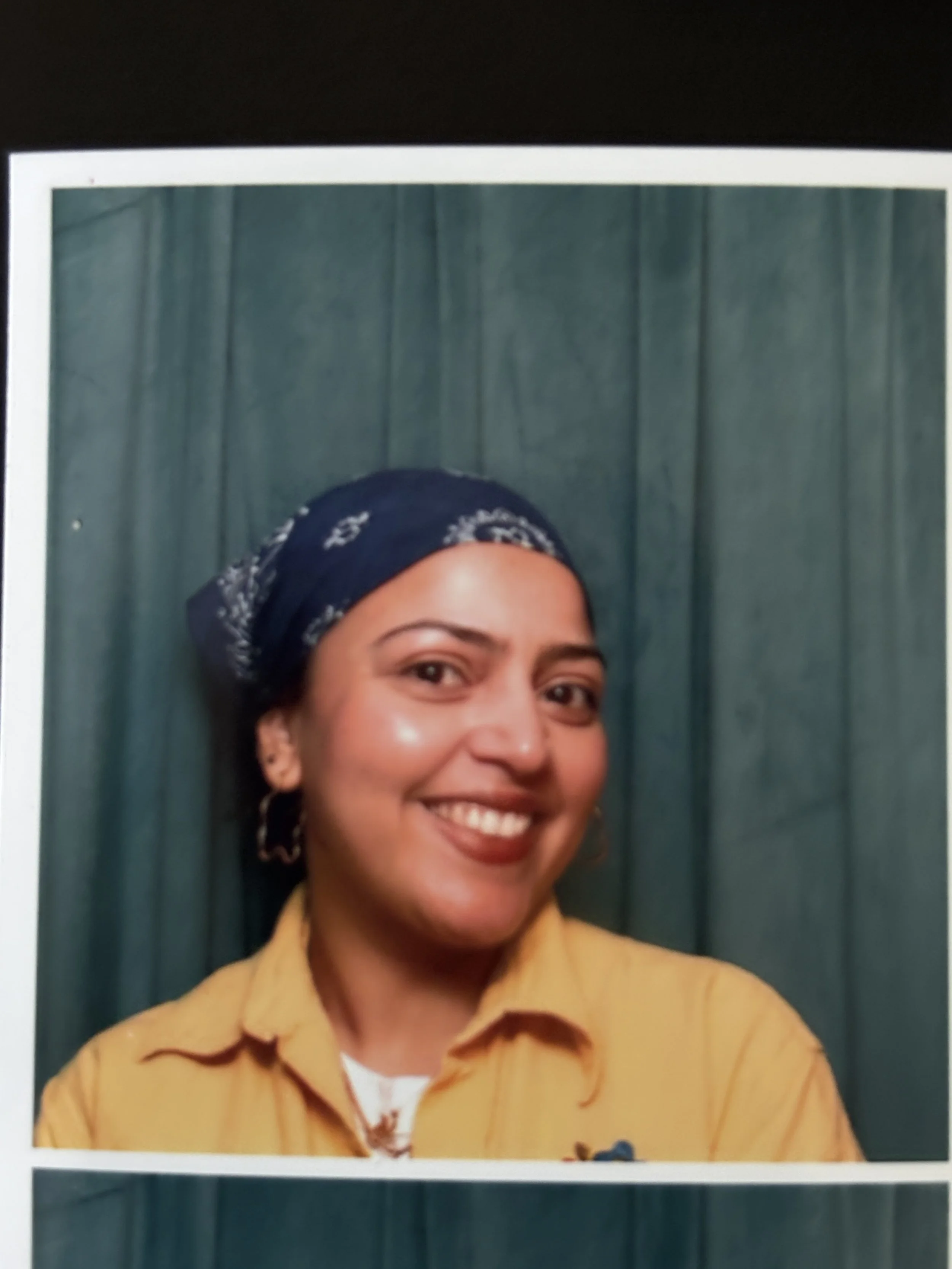 A person wearing a bandana headband and a yellow button down shirt smiles for the camera