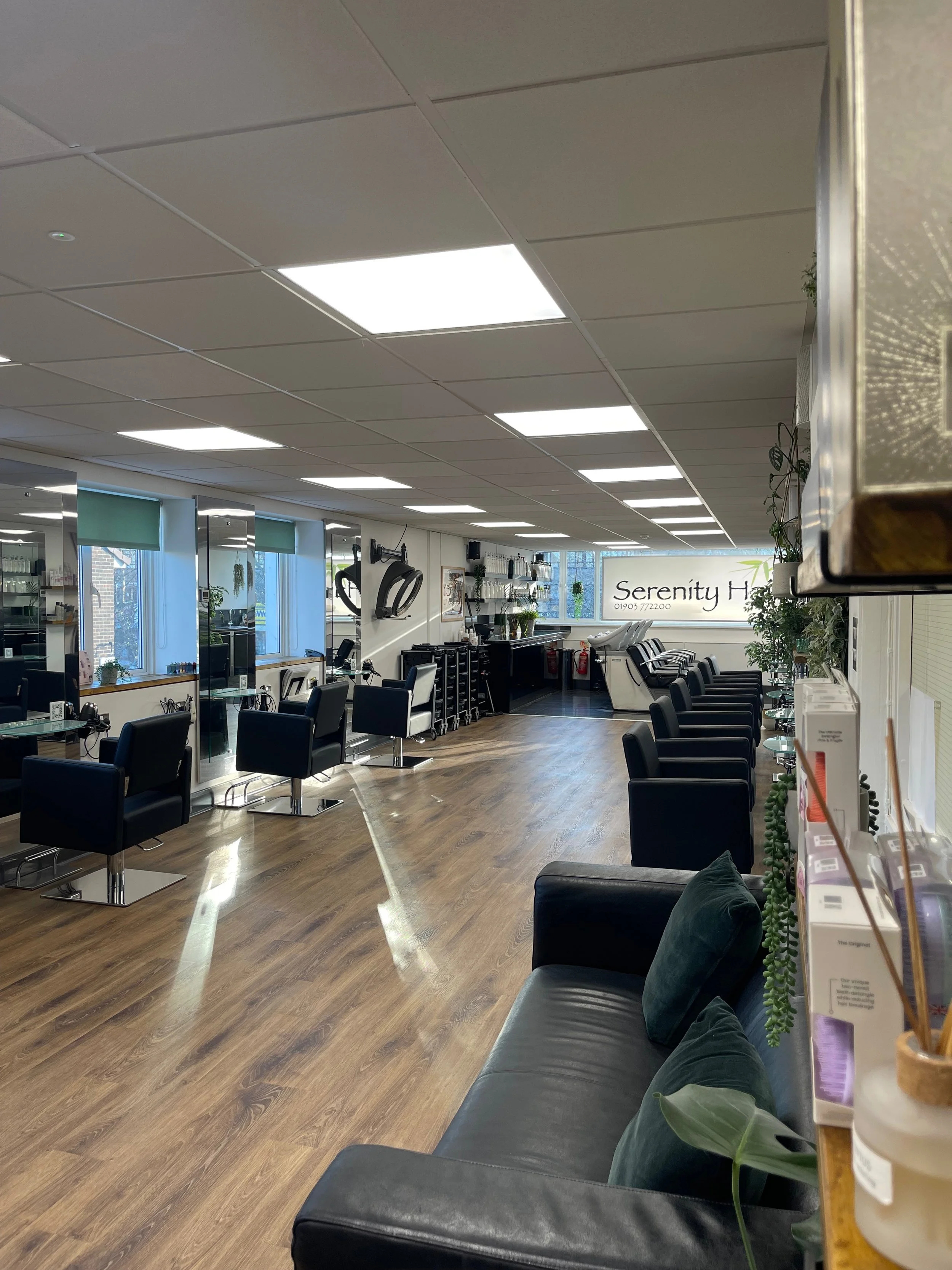 Interior of a hair salon named Serenity Hair with salon chairs, mirrors, and hair styling stations, along with greenery and natural light from windows.