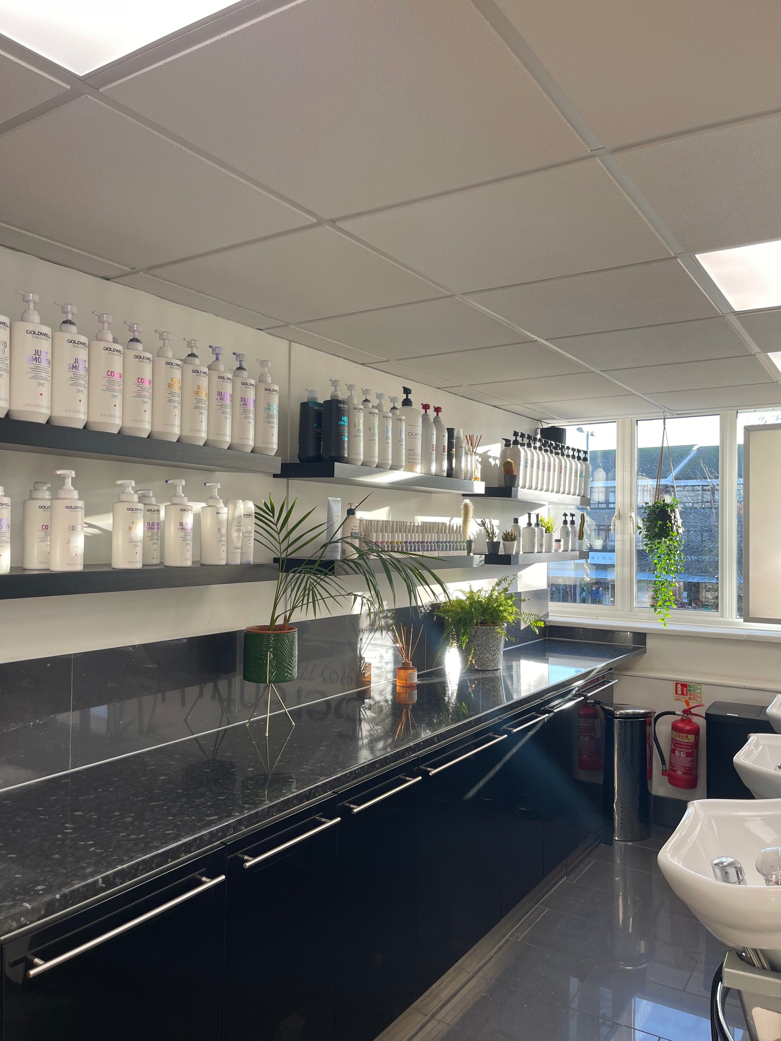 Image of a hair salon shampoo station featuring shelves of hair care products on the wall.