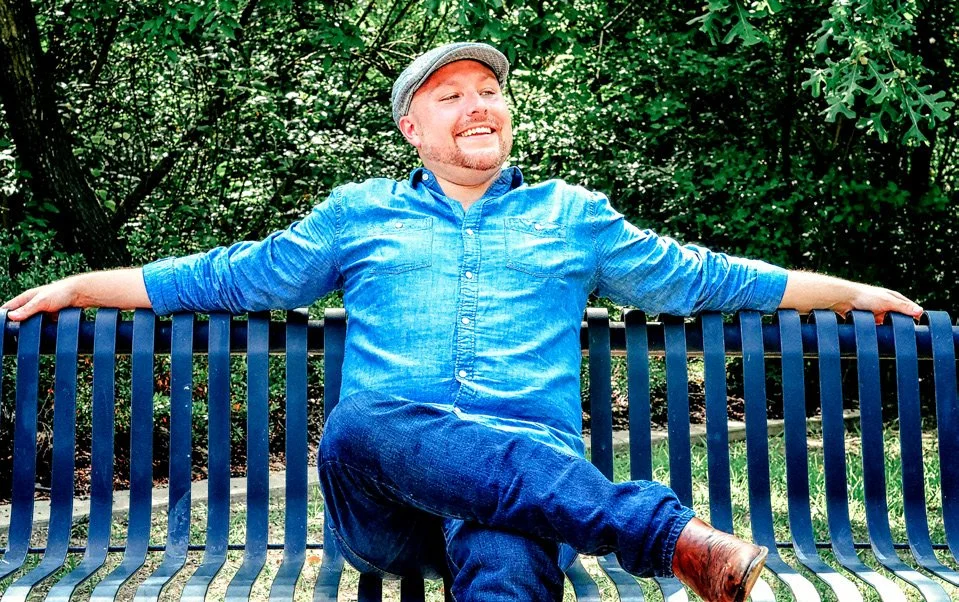Tenor Dustin Lucas smiling on a park bench