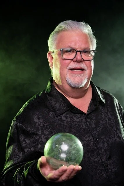 Middle-aged white man, dressed in black, holding a crystal ball
