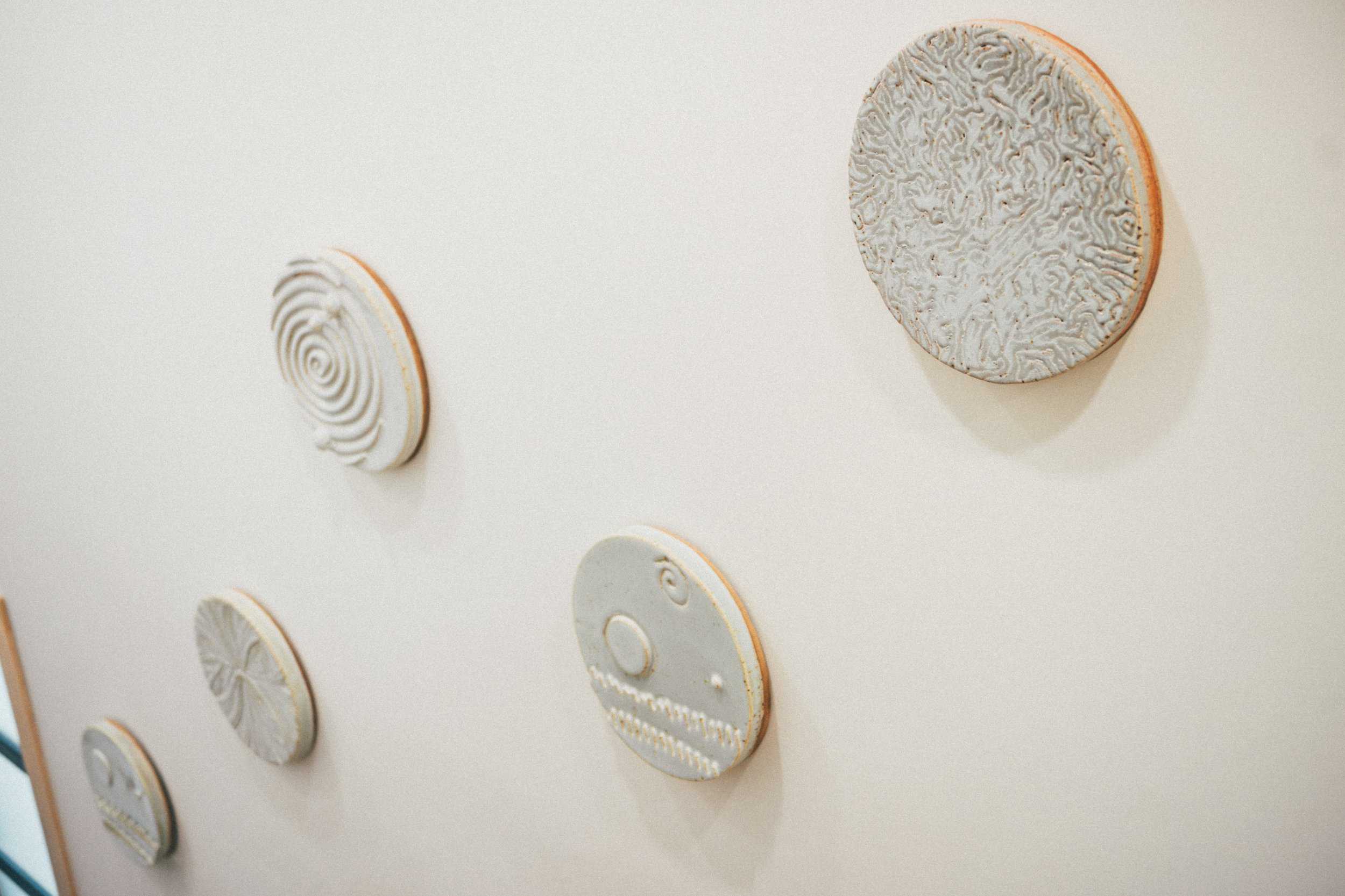Wall display of multiple round, textured ceramic plates with different patterns, some featuring spiral or swirl designs.