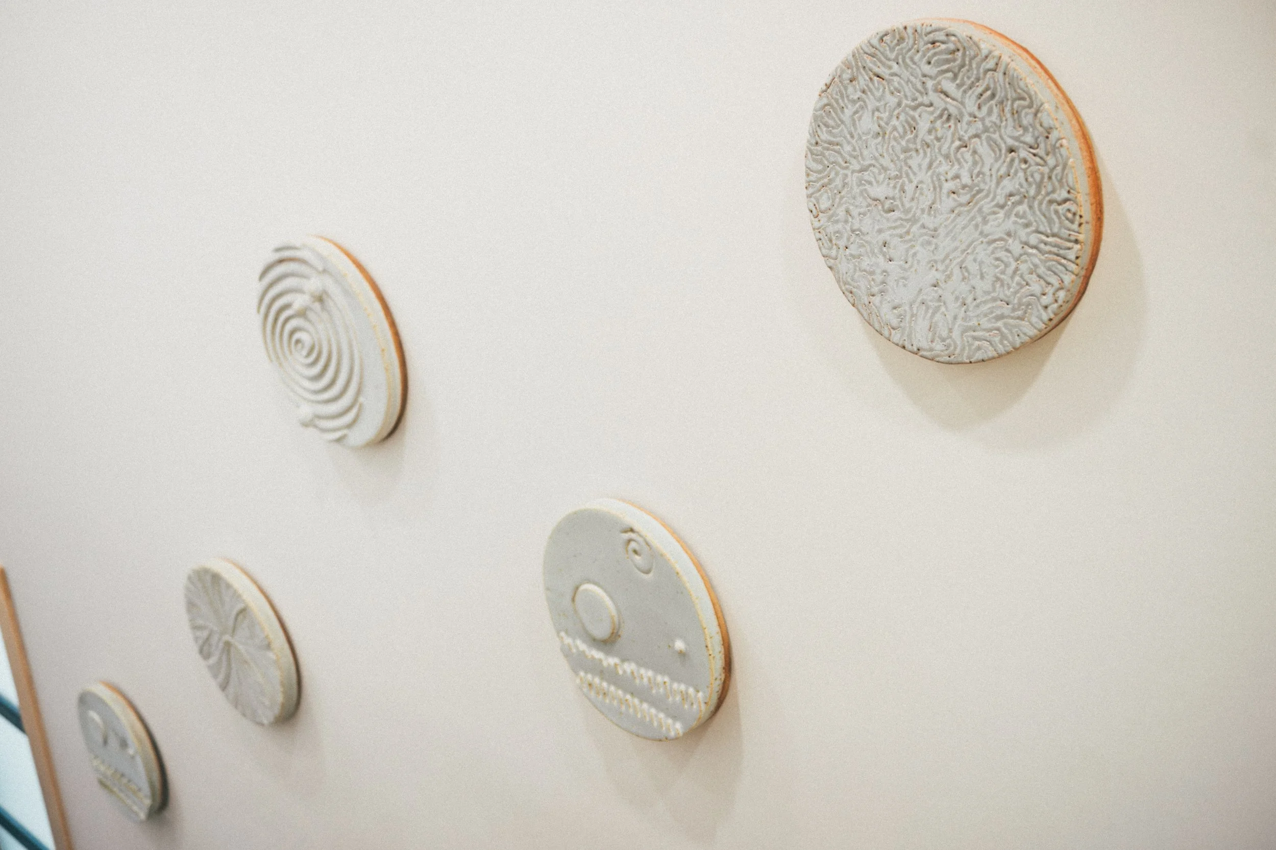 Wall display of multiple round, textured ceramic plates with different patterns, some featuring spiral or swirl designs.