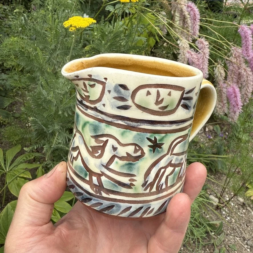 pot3037 - Milk jug with dog and cats and smiley suns. Caramel glaze inside and on handle.