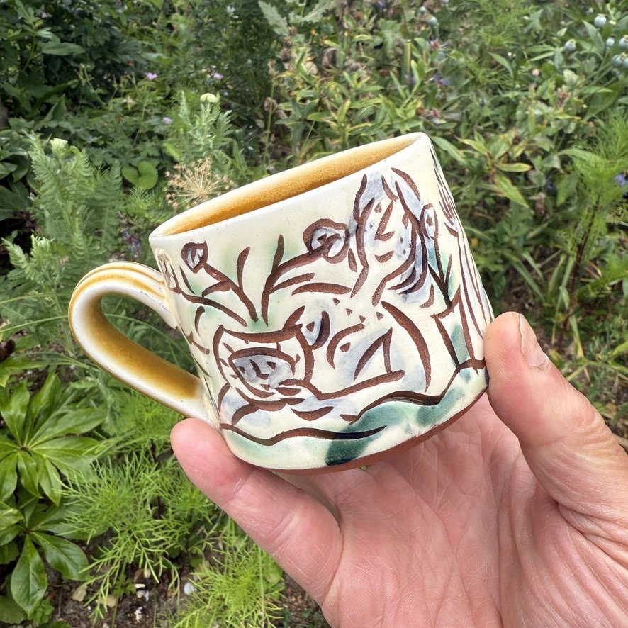 pot2995 Slipware medium coffee mug with gardening folk. Signature on base. Caramel glaze on handle and inside.