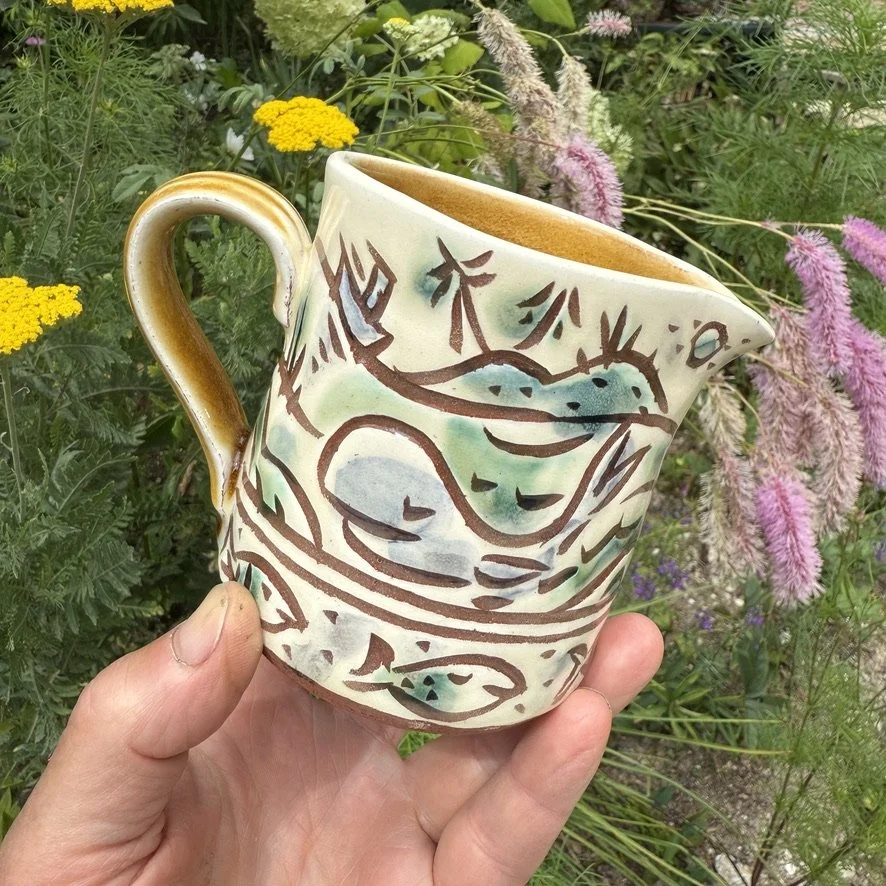 pot3038 - Milk jug with whale and fish in a Norwegian bay. Caramel coloured glaze onside and on handle.