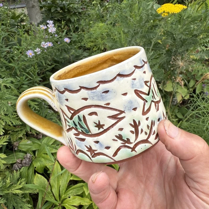 pot3049 Medium coffee mug with fishys border. Signature on base. Caramel glaze on handle and inside.