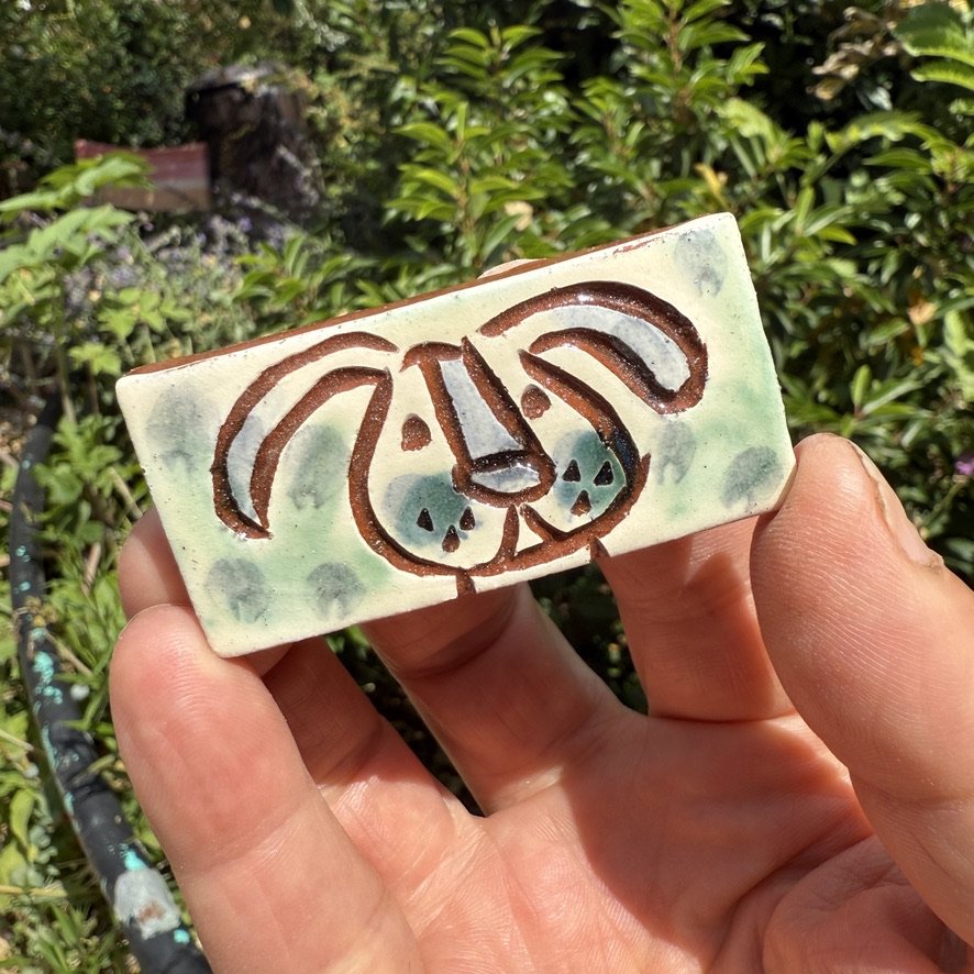 pot2983 Small rectangular tile with dog face.