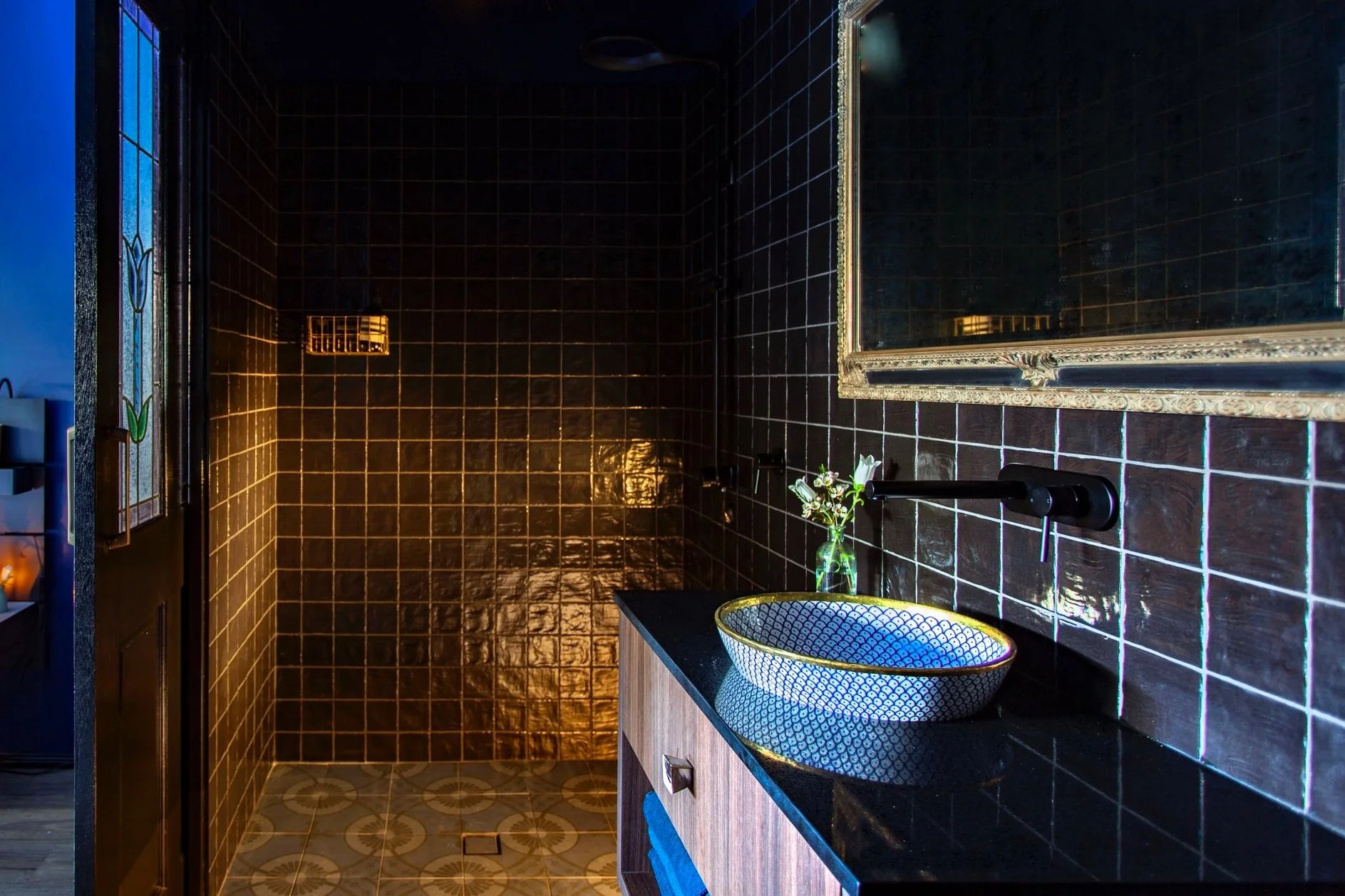 Indulge in luxury at my designer bathroom featuring handpicked treasures from around the world, including 1200 square black tiles from Spain, a hand-painted sink from Morocco, and a stunning antique mirror found in country NSW. The unique lighting fi